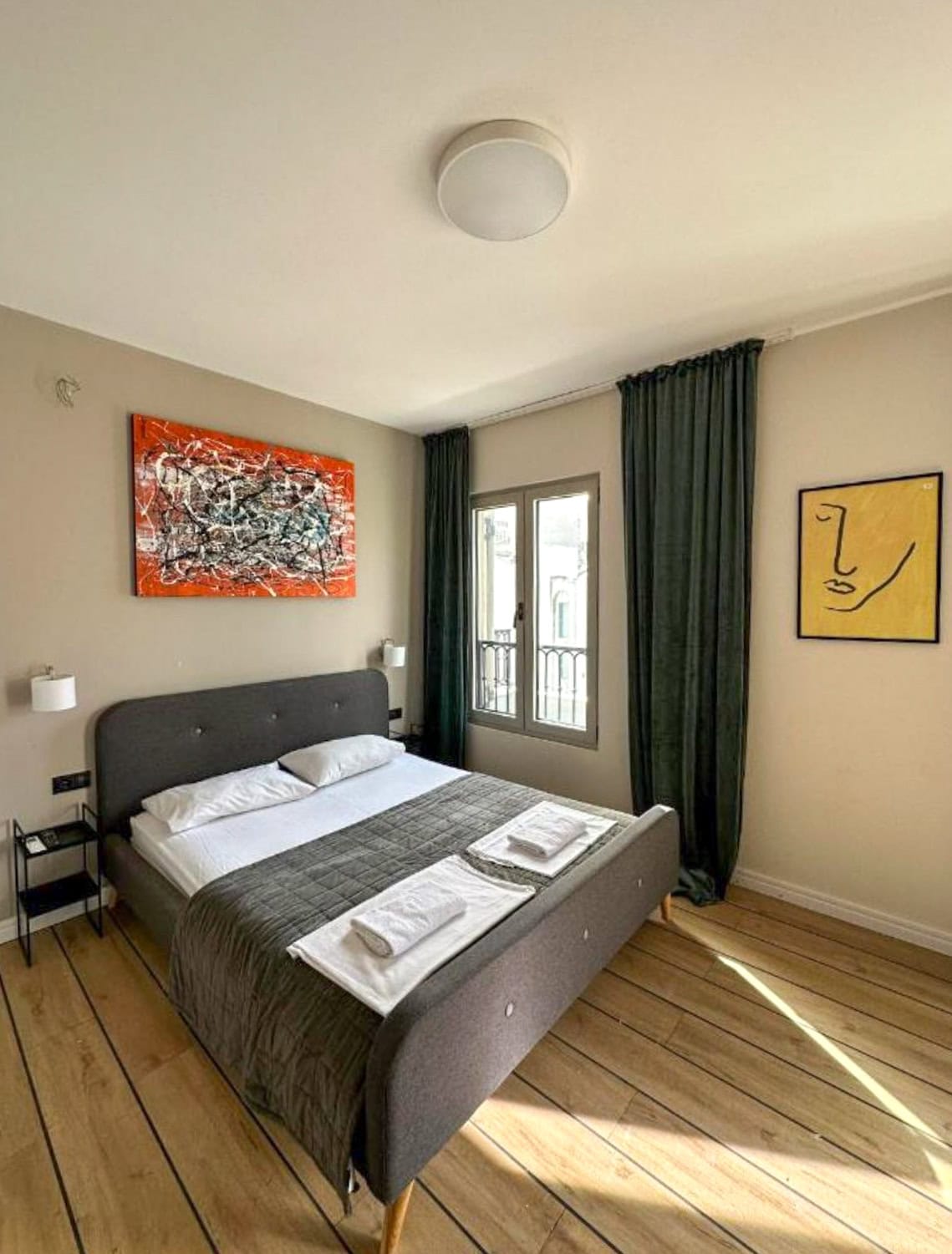 Modern bedroom with a double bed in an apartment in Budva, Montenegro: stylish decor, parquet flooring, and dark curtains.
