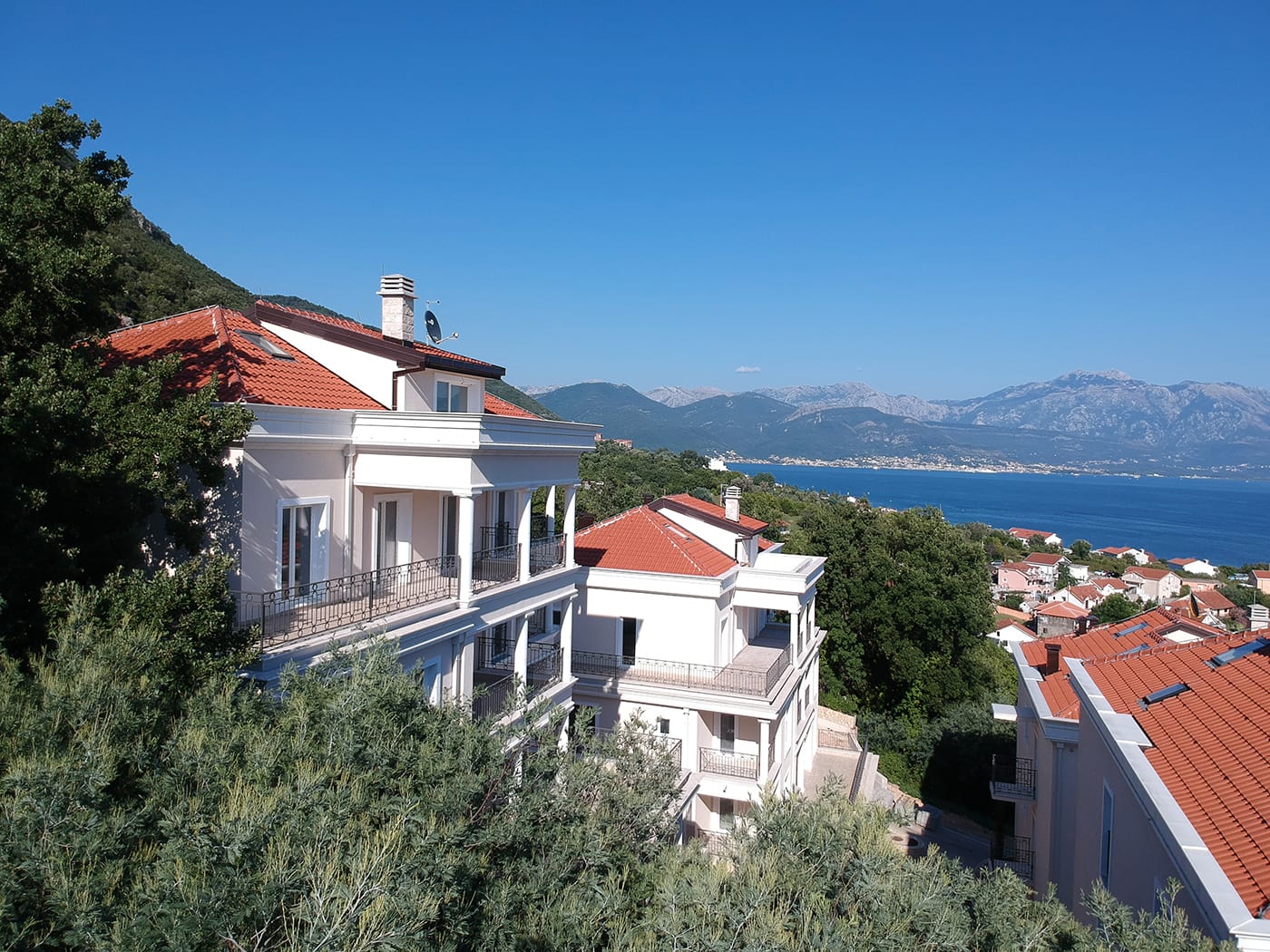 Modern villas with red roofs and sea views in Kumbor, Montenegro, surrounded by greenery and mountains.