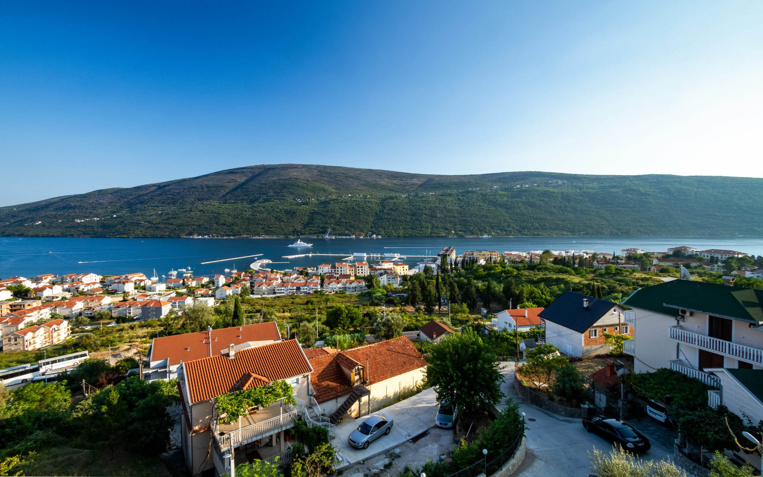 Panoramic view of the sea, the bay, and a residential complex in Kumbor, Montenegro: houses with tiled roofs and mountains in the background.