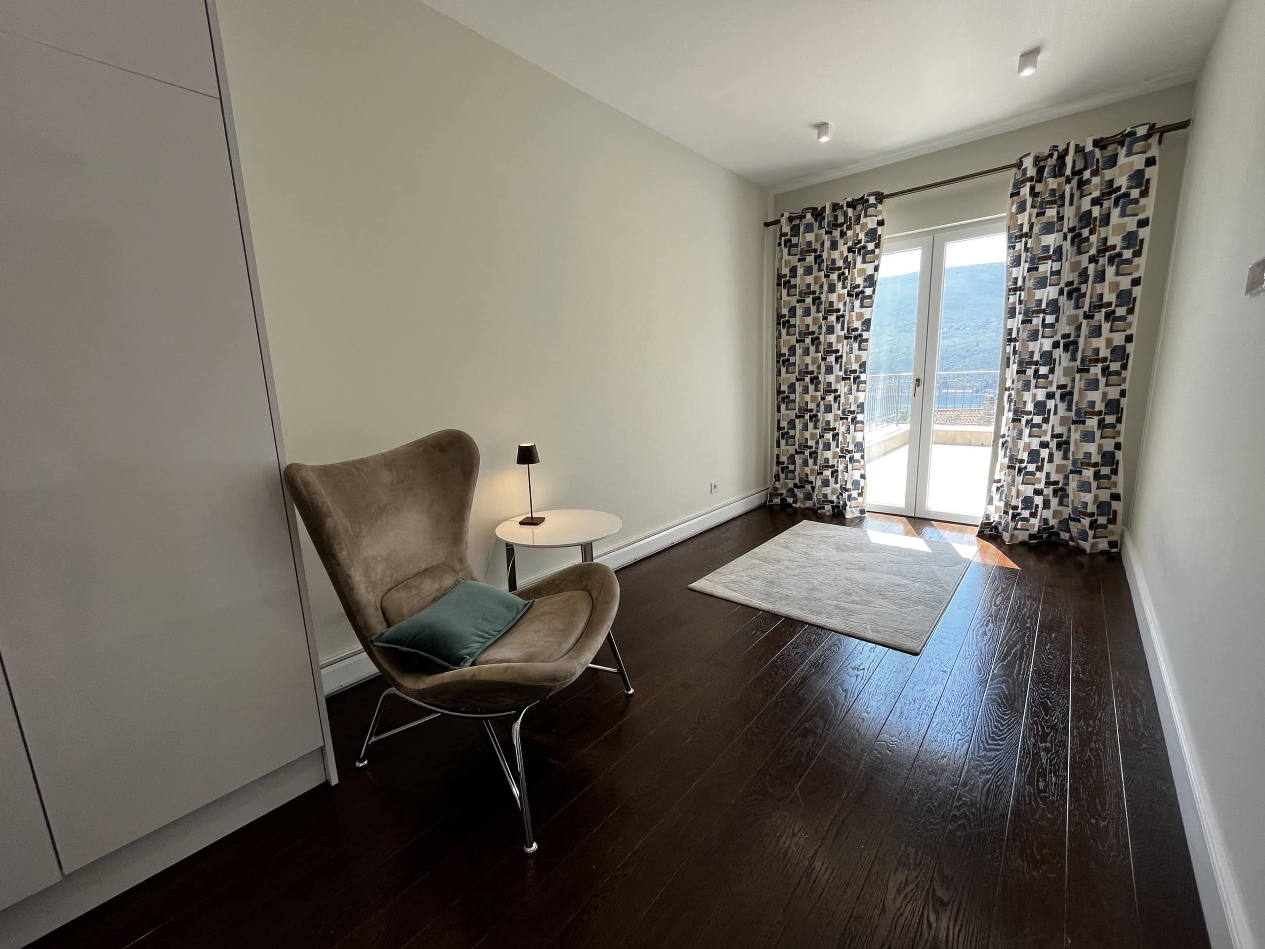 Living room in Kumbor residential complex, Montenegro: modern interior, dark parquet flooring, armchair, access to a terrace with sea view.