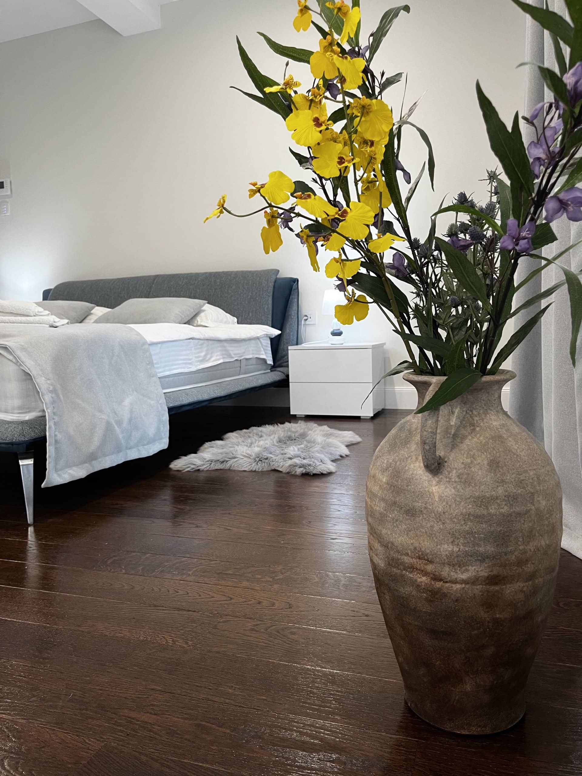 Cozy bedroom in the Kumbor residential complex, Montenegro: double bed, dark parquet flooring, and a stylish vase with flowers in the interior.