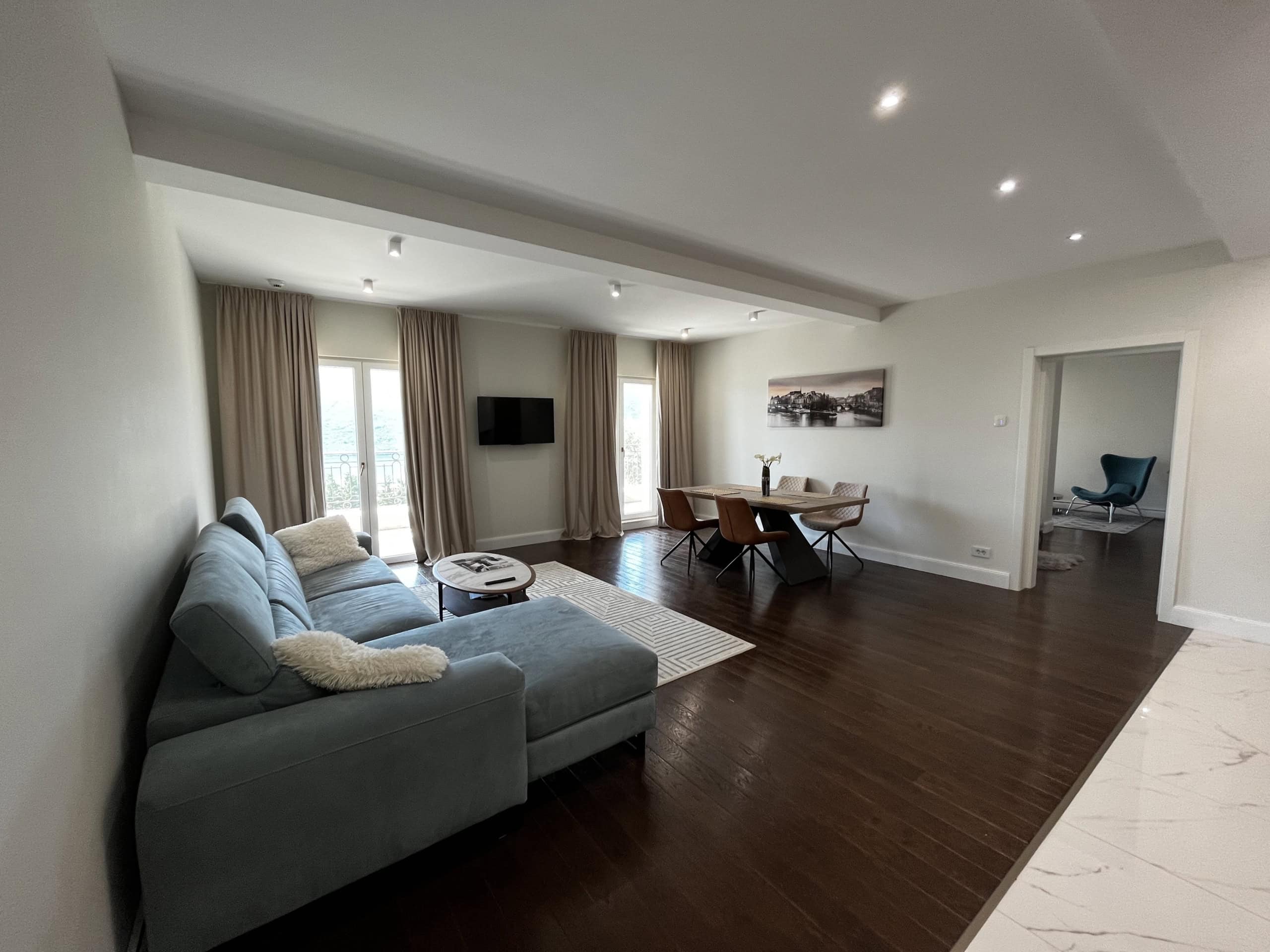 Spacious living room with a blue sofa and dining area in a residential complex in Kumbor, Montenegro: modern interior, parquet flooring.