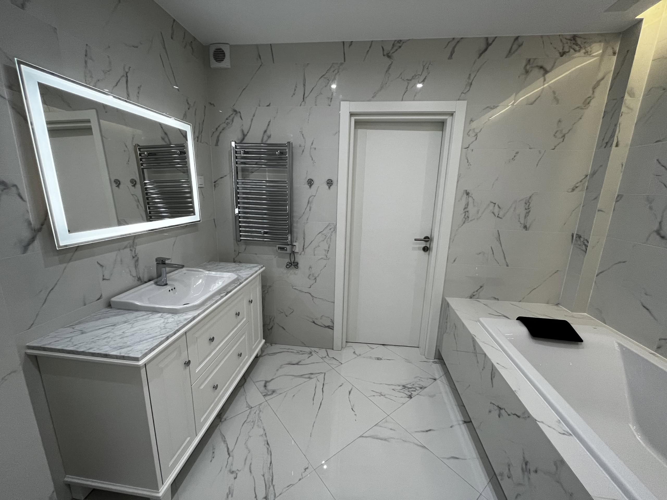 Modern bathroom with marble-look finishes in Kumbor residential complex, Montenegro: vanity with sink and illuminated mirror.