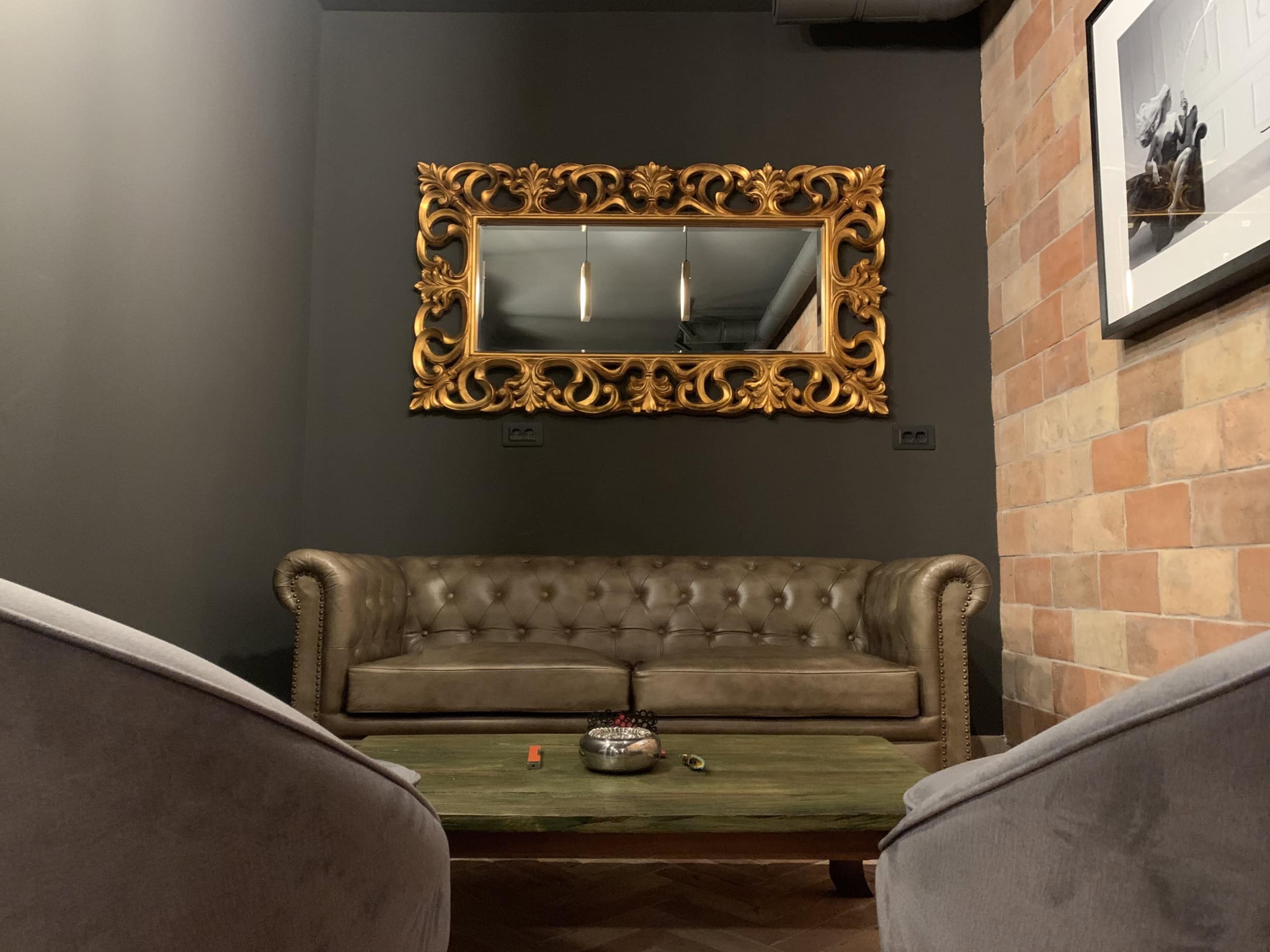 Living room in Kumbor residential complex, Montenegro: Chesterfield leather sofa, gold mirror, and brick wall finish in the interior.
