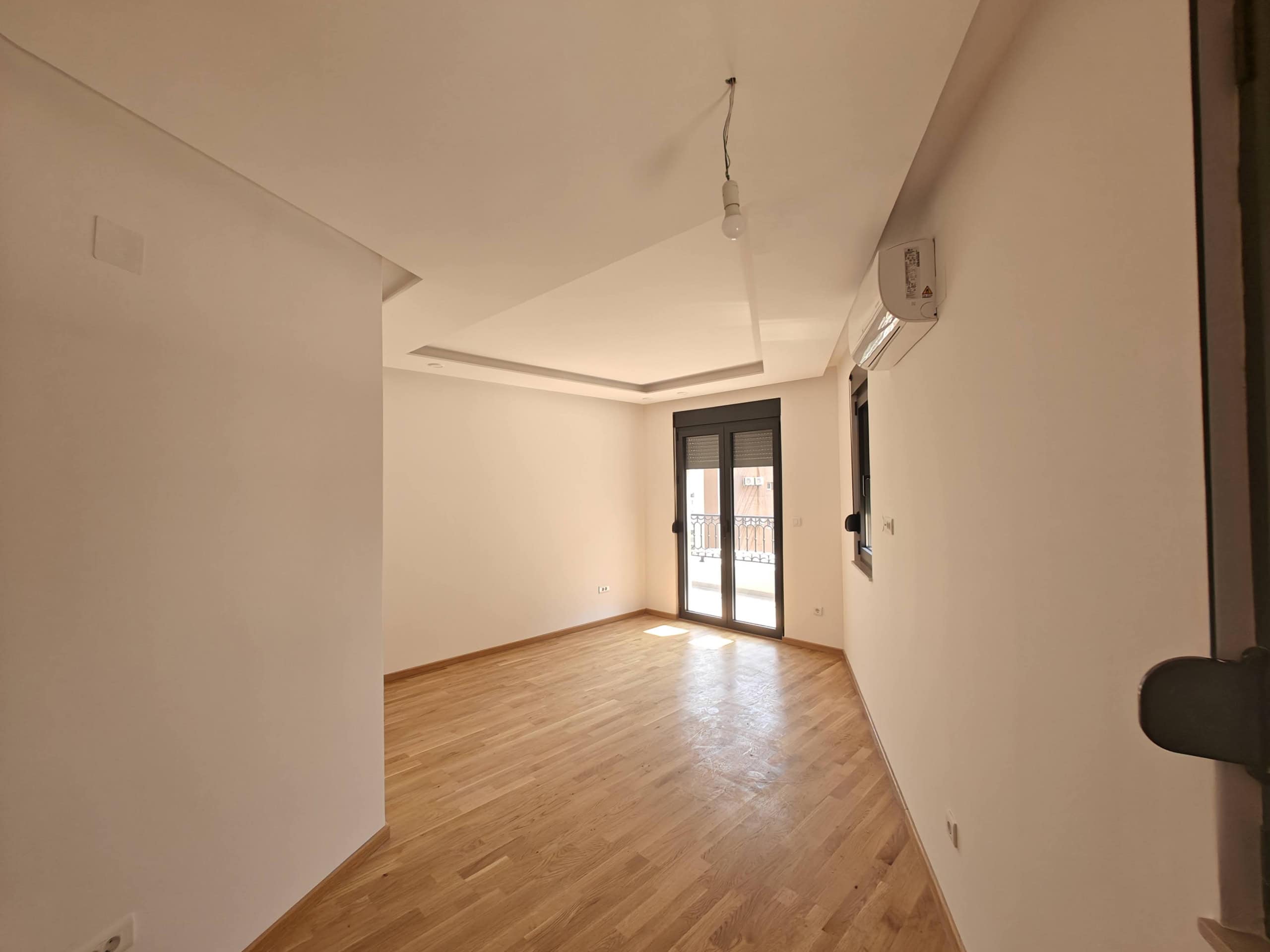 Bright living room with parquet flooring, air conditioning, and access to the balcony in a new apartment, Budva, Montenegro.