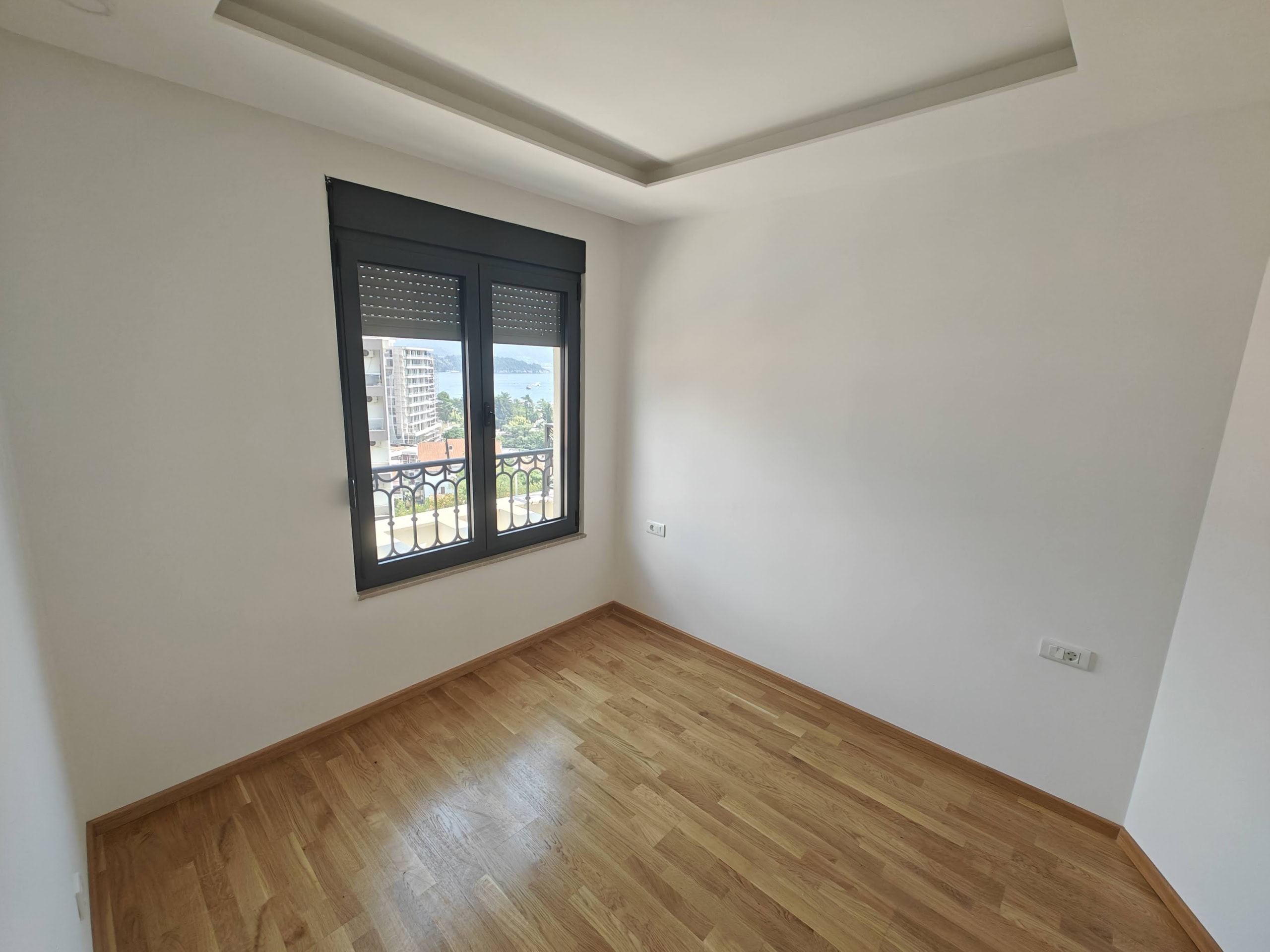 Bright bedroom with parquet flooring and sea view in an apartment in Budva, Montenegro. Modern finishes, window with roller shutters.