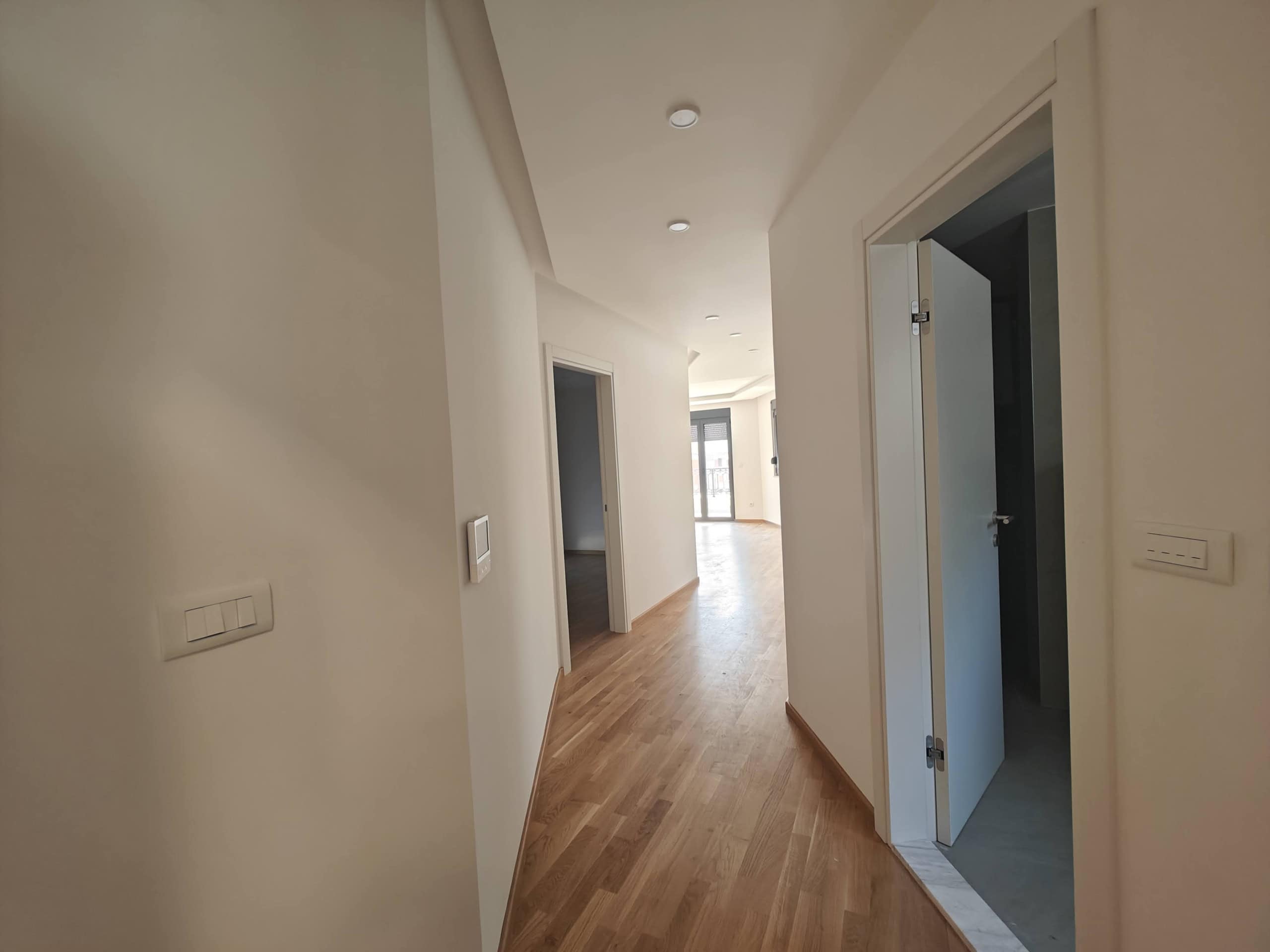 Bright hallway in a modern apartment in Budva, Montenegro: parquet flooring, white walls, and built-in lighting.