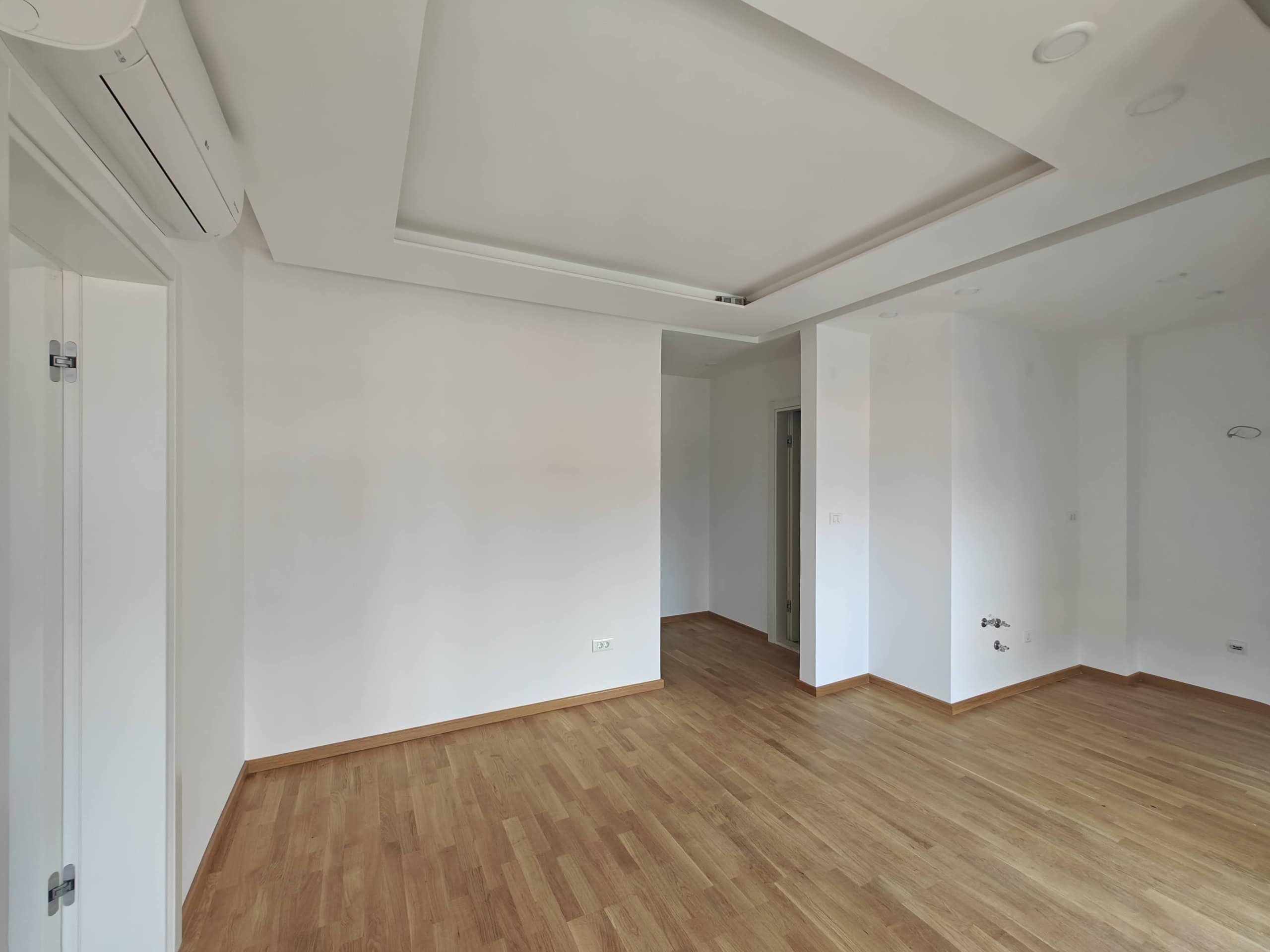 Bright living room in an apartment in Budva, Montenegro: parquet floor, multi-level ceiling, and installed air conditioner.