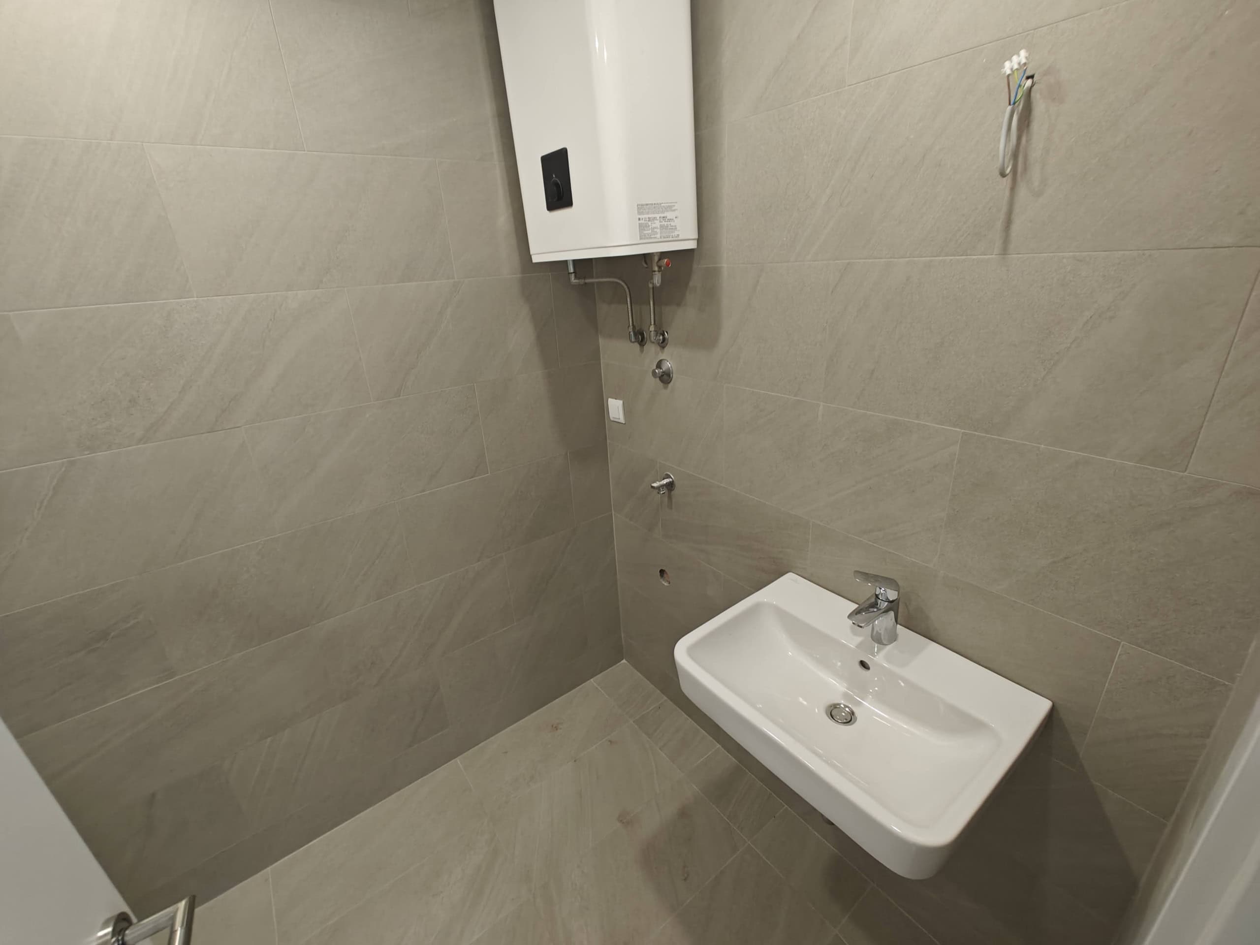 Modern bathroom in an apartment in Budva, Montenegro: beige tiles, wall-mounted water heater, and wall-hung sink.