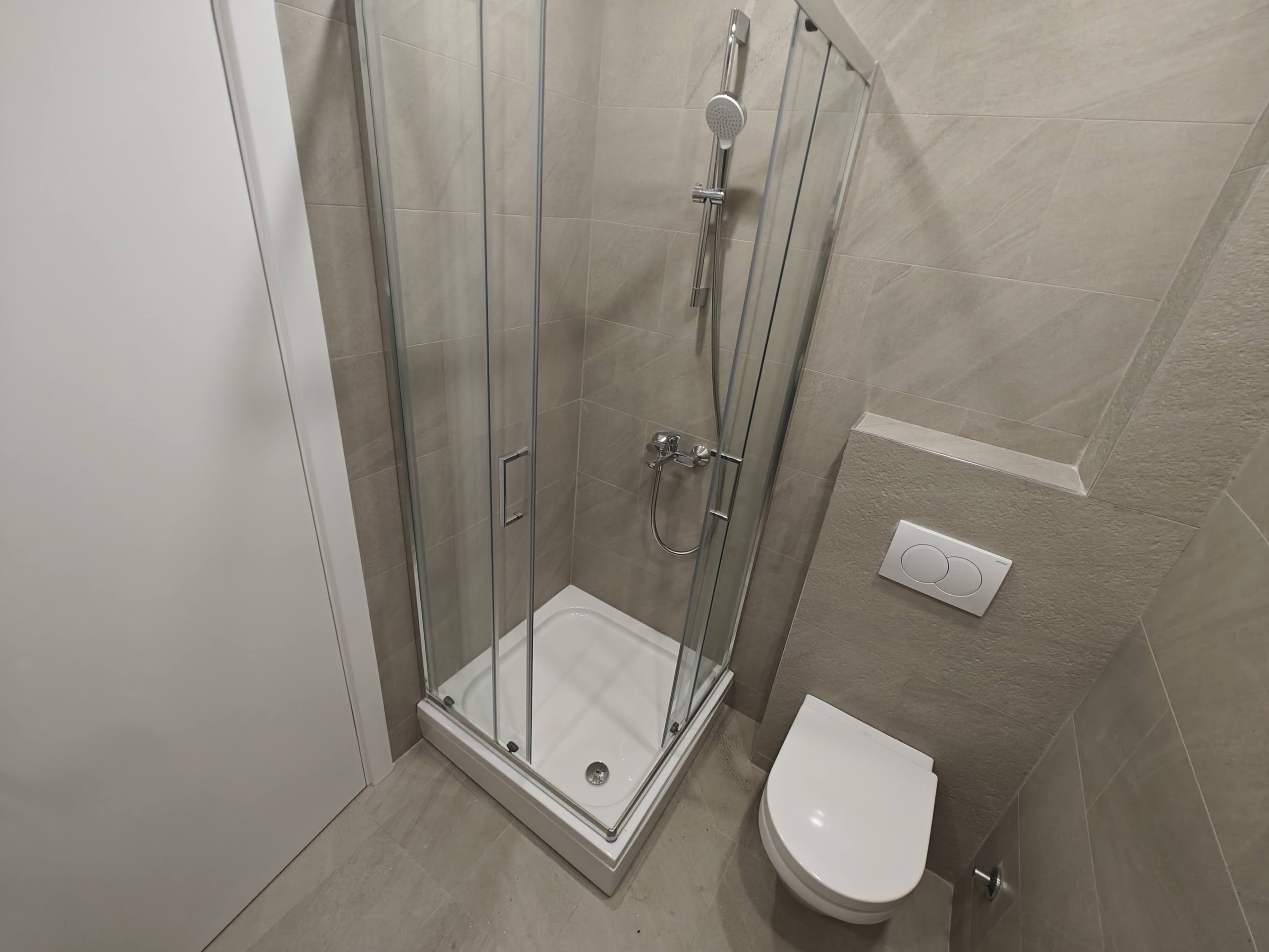 Modern bathroom in an apartment in Budva, Montenegro: shower cabin, wall-mounted toilet, and beige tiles.