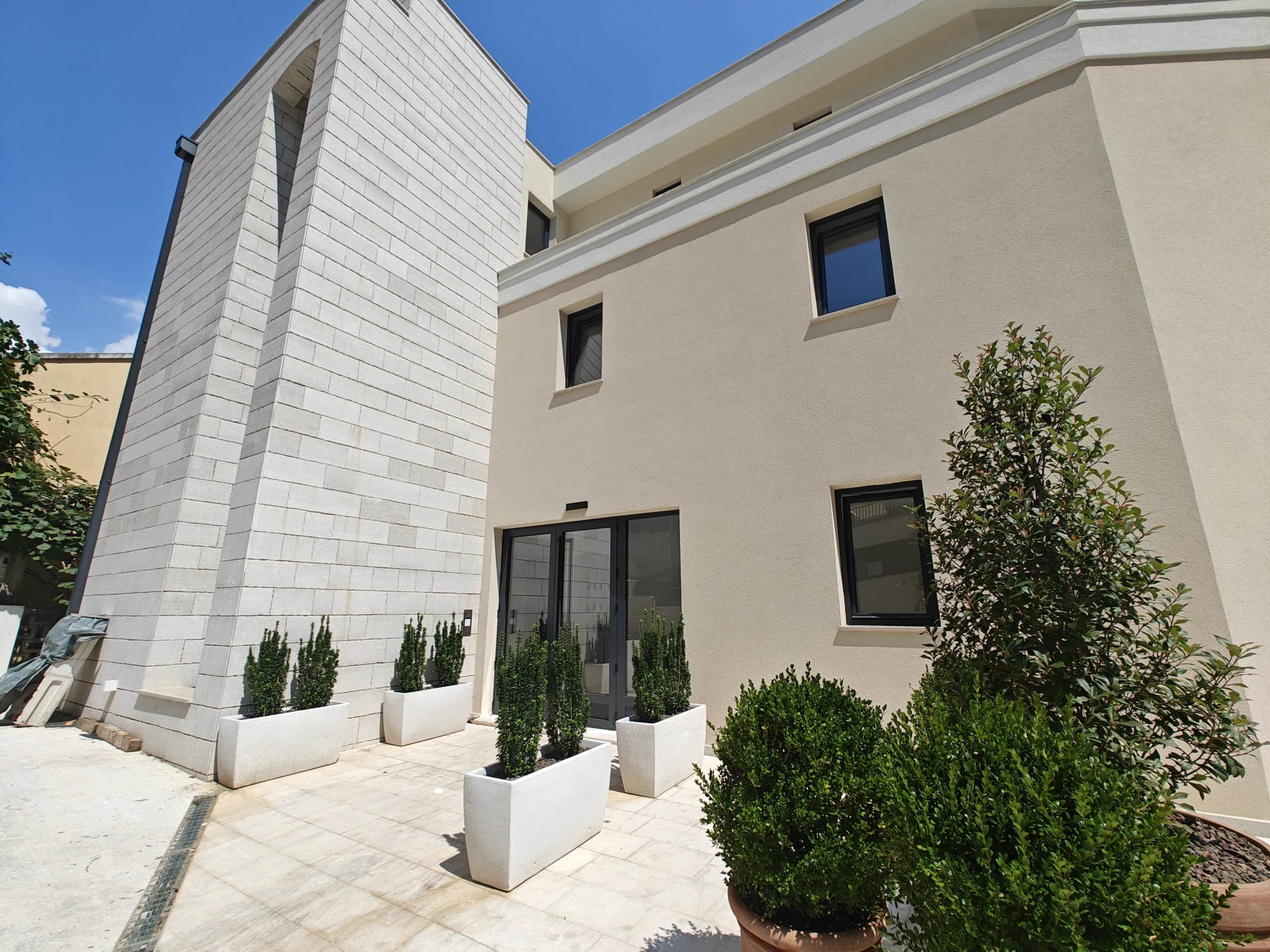 Modern facade of a residential building in Budva, Montenegro, with stone cladding, panoramic windows, and a terrace with plants.