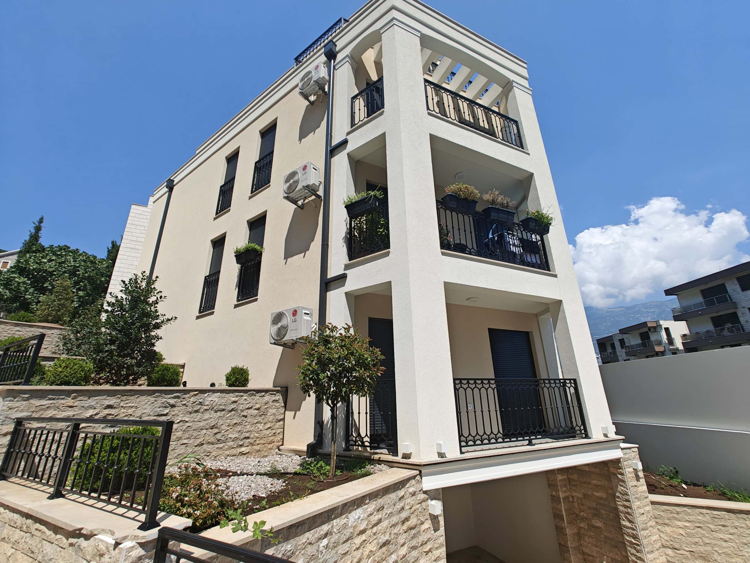 Three-story residential house in Budva, Montenegro: modern facade with balconies, wrought-iron railings, and landscaping.