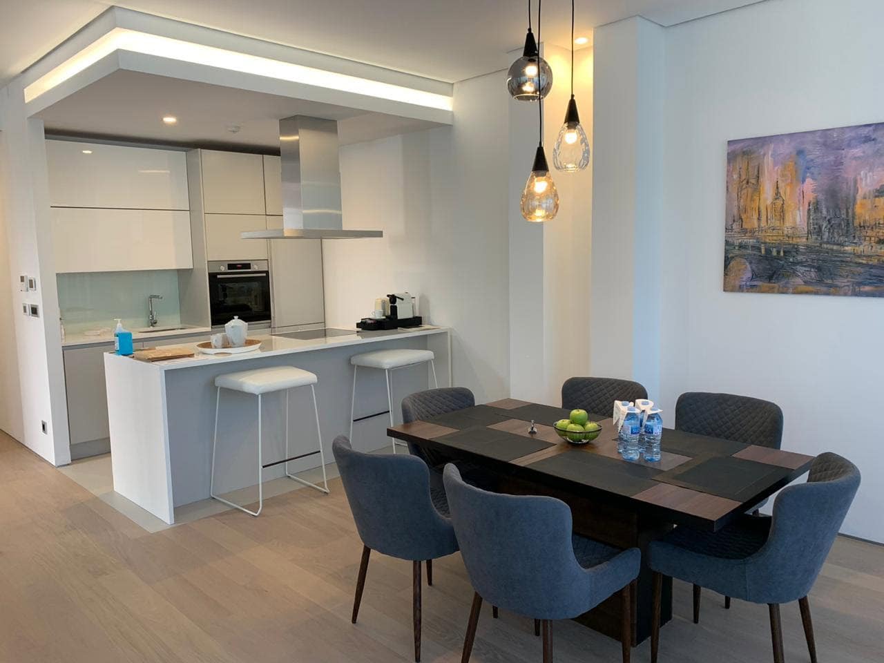 Modern kitchen-dining room in Budva residential complex, Montenegro: white furniture, breakfast bar, dining area with gray chairs.