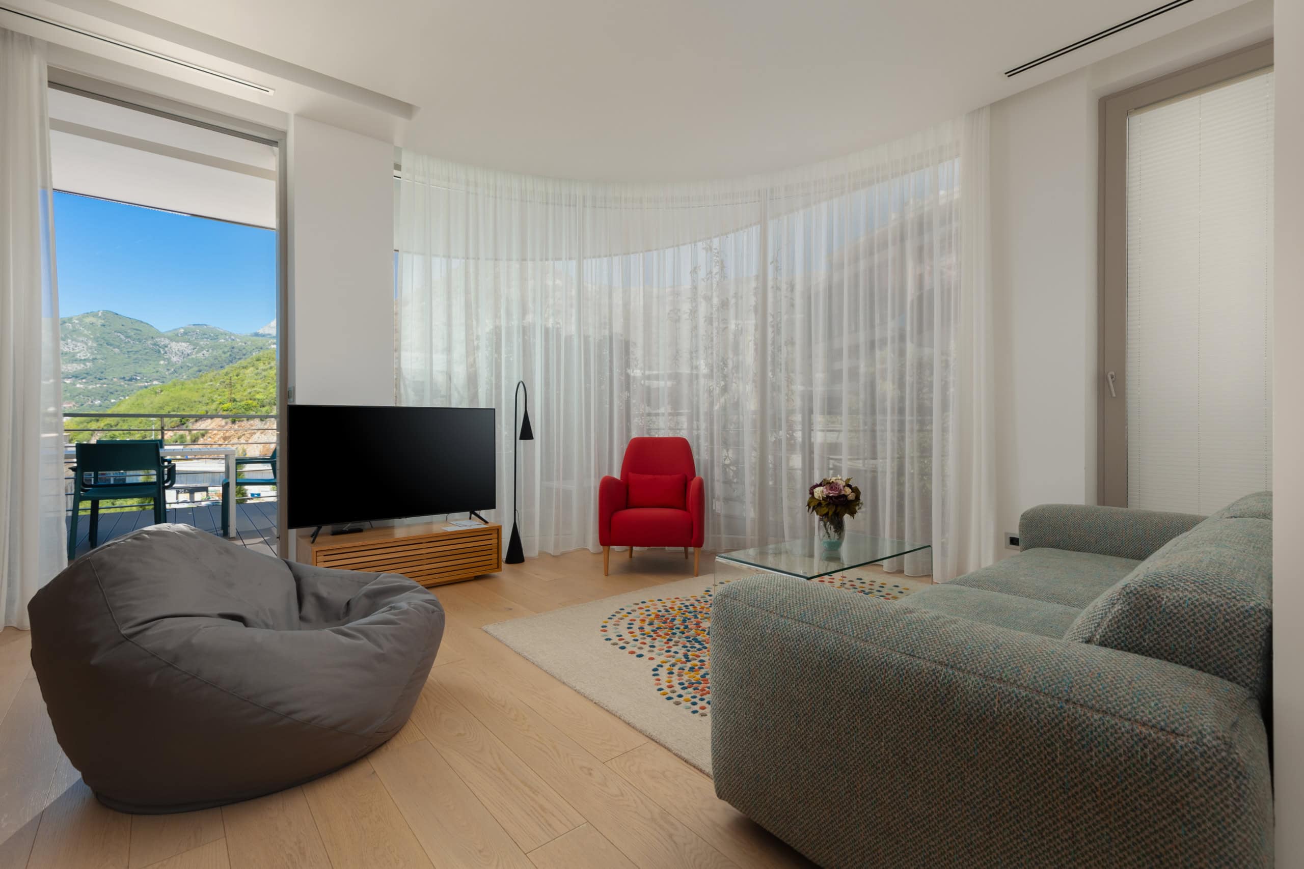 Modern living room in ЖК Budva, Montenegro: panoramic windows, mountain view, stylish furniture, and access to the terrace.