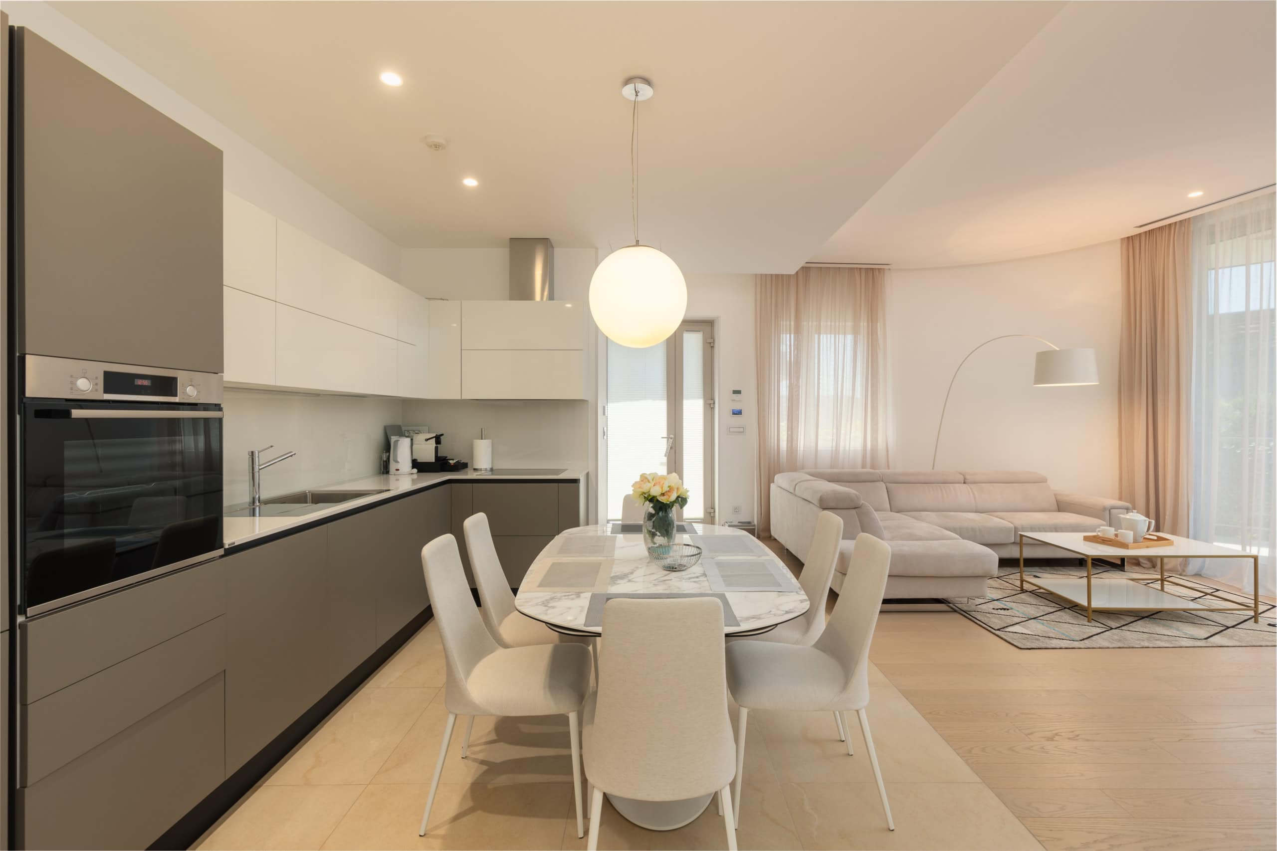 Modern kitchen-living room with dining area in a residential complex in Budva, Montenegro: bright interior, soft furnishings, and appliances.