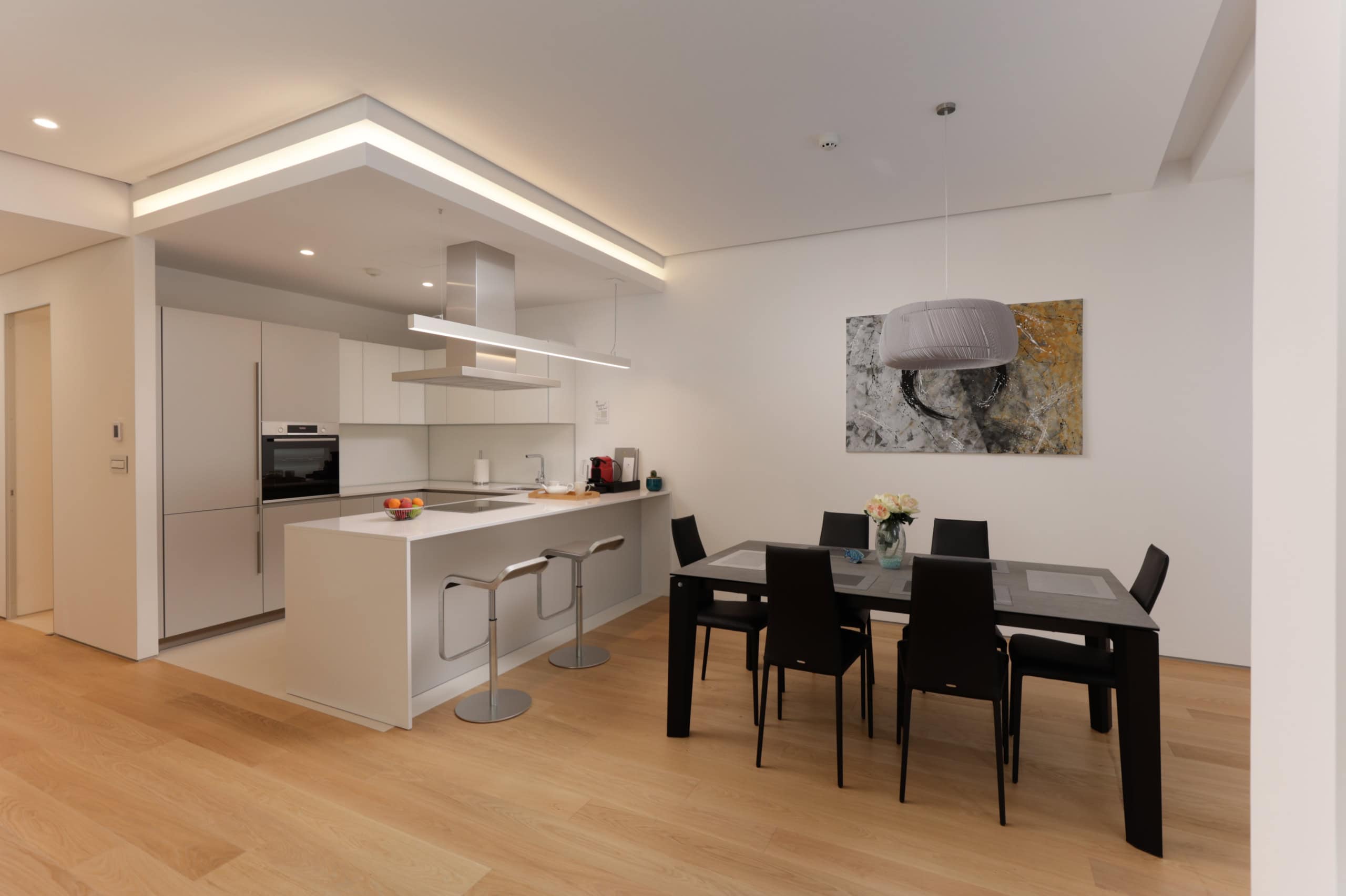 Modern kitchen-dining room in Budva residential complex, Montenegro: white furniture, an island with bar stools, and a dining area.