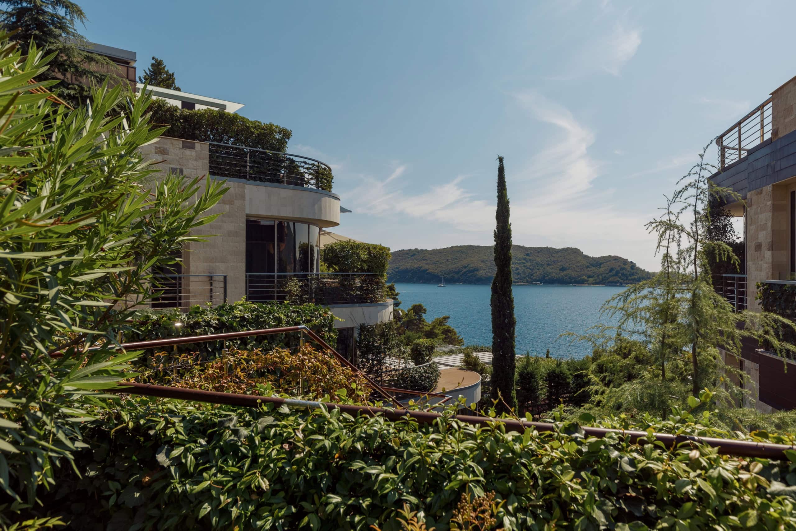 Modern villa with terraces and panoramic sea views in Budva, Montenegro, surrounded by greenery and cypress trees.