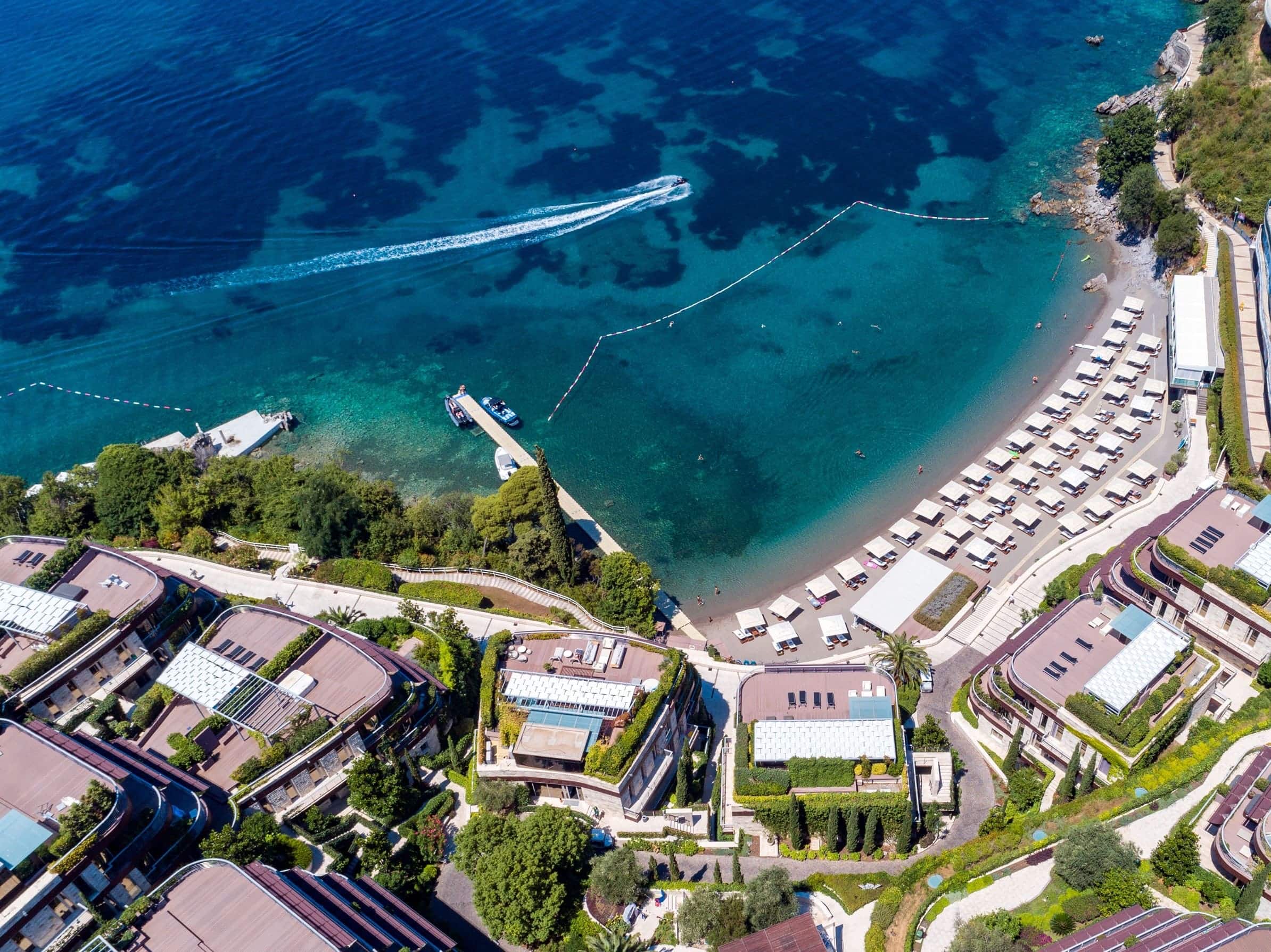 Aerial view of a luxury residential complex in Budva, Montenegro, with a private beach and yacht pier.