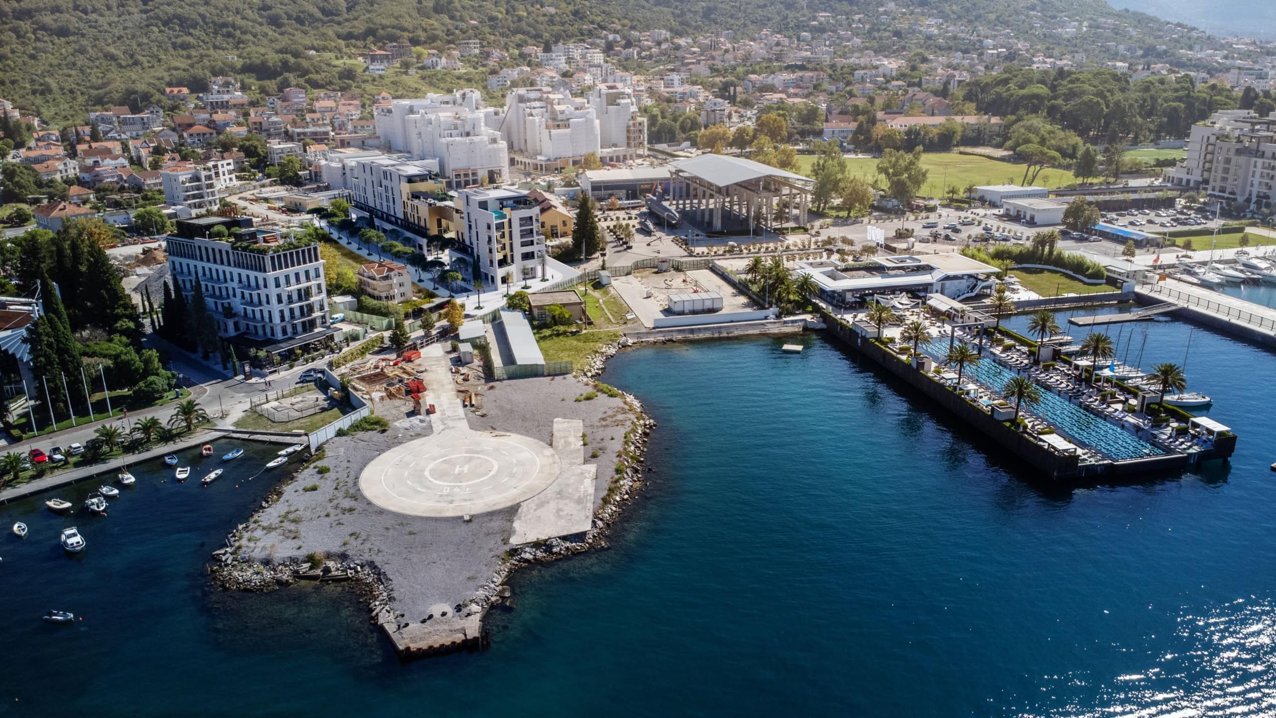 Aerial view of a residential complex in Tivat, Montenegro: a helipad, a seaside pool, and modern architecture.