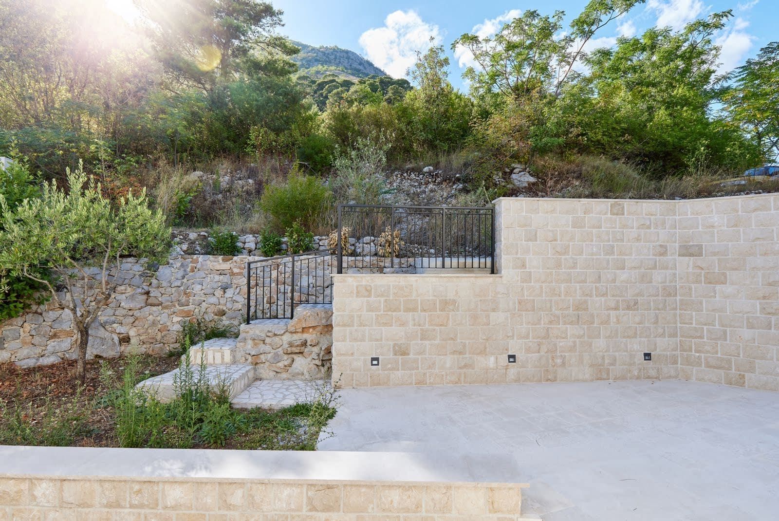 Villa terrace in Prčanj, Montenegro: stone masonry, staircase with wrought-iron railings, and landscaped grounds.