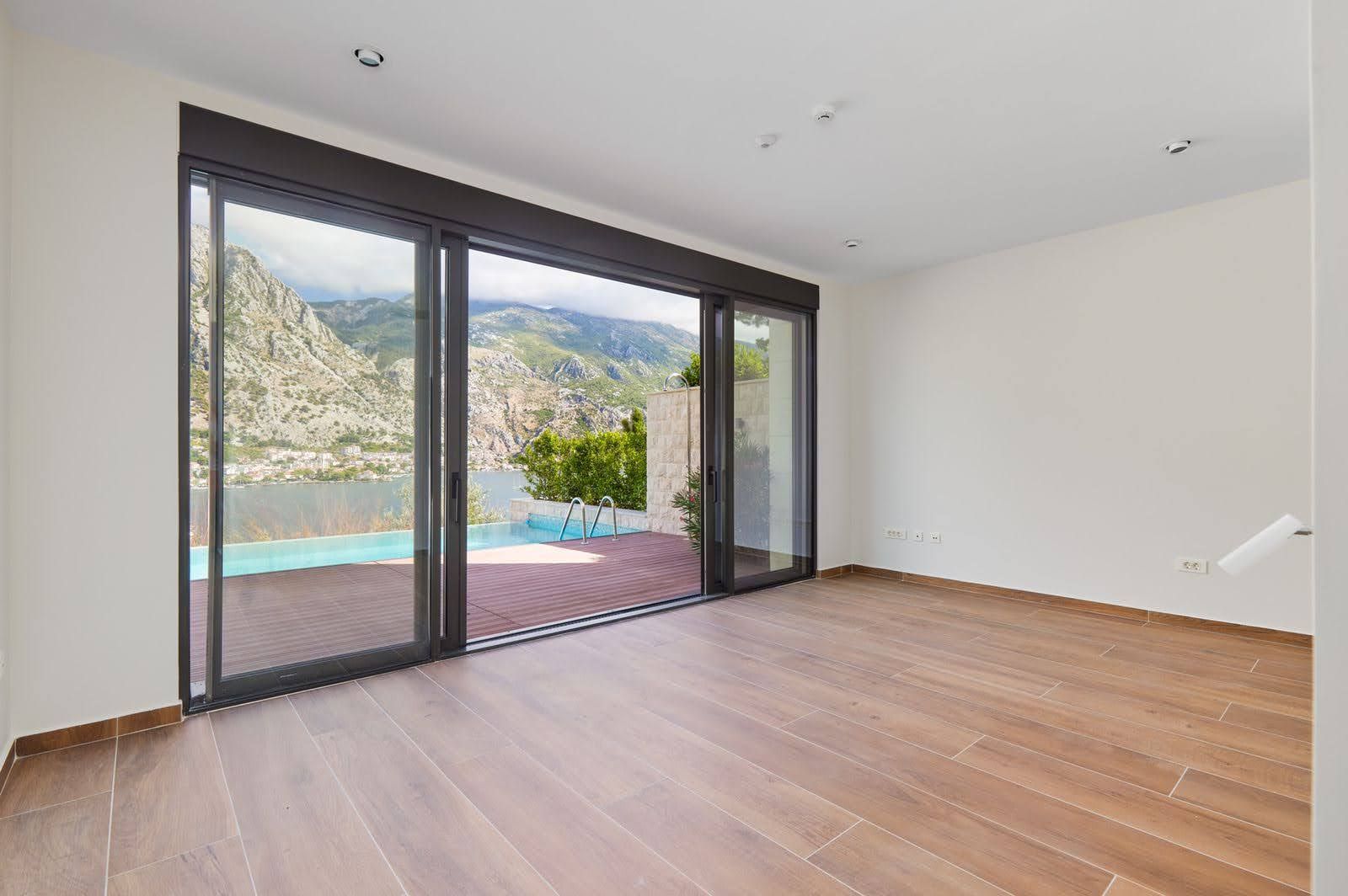Living room in a villa in Prčanj, Montenegro: panoramic windows, views of the Bay of Kotor, mountains, and a private pool.
