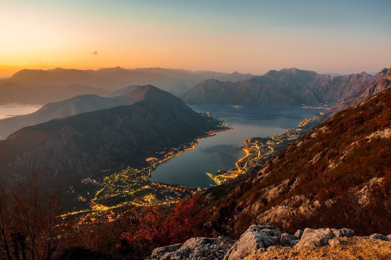 Panoramic view of Kotor Bay and the town of Prčanj in Montenegro at sunset, seen from the mountain with the coastal lights at night.