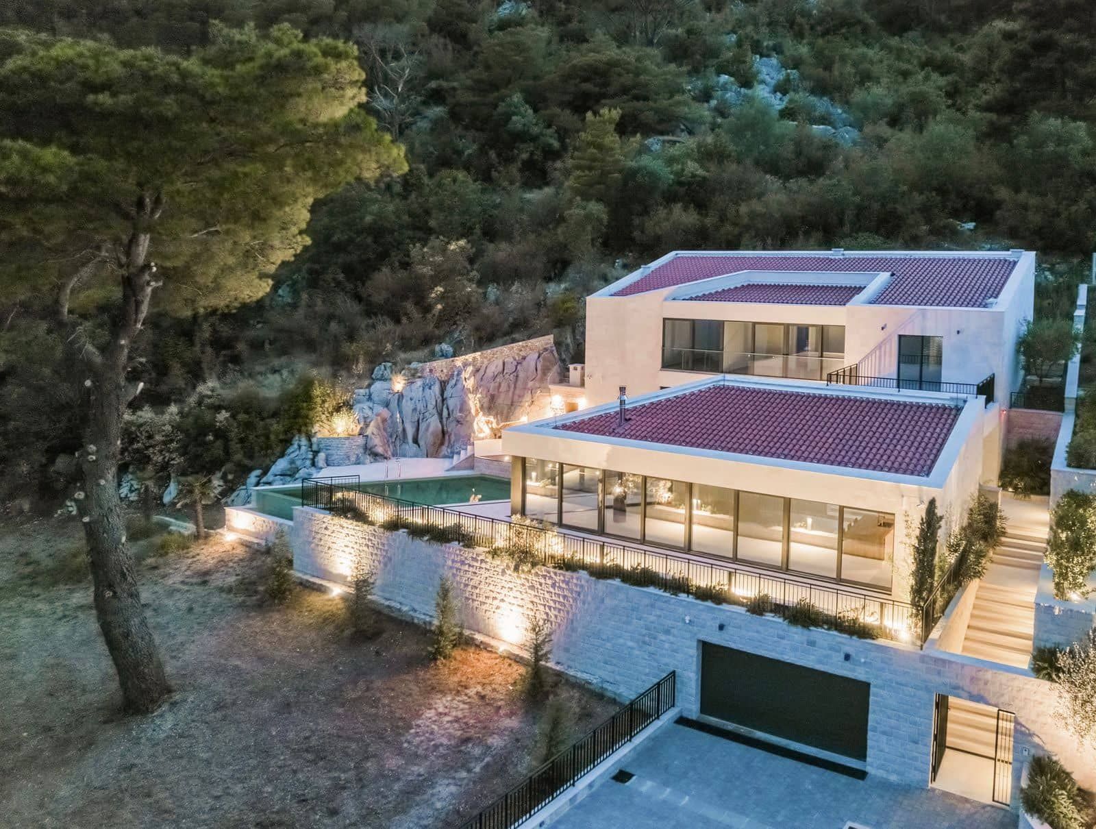 Modern villa with a pool and panoramic windows in Prčanj, Montenegro: exterior view with lighting and a terrace.