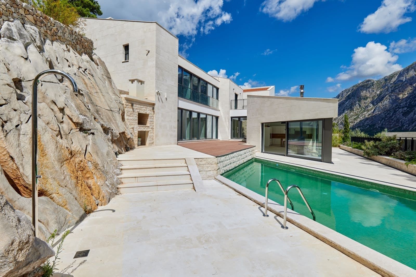 Modern villa in Prčanj, Montenegro: pool, stone facade, terrace, and mountain view.