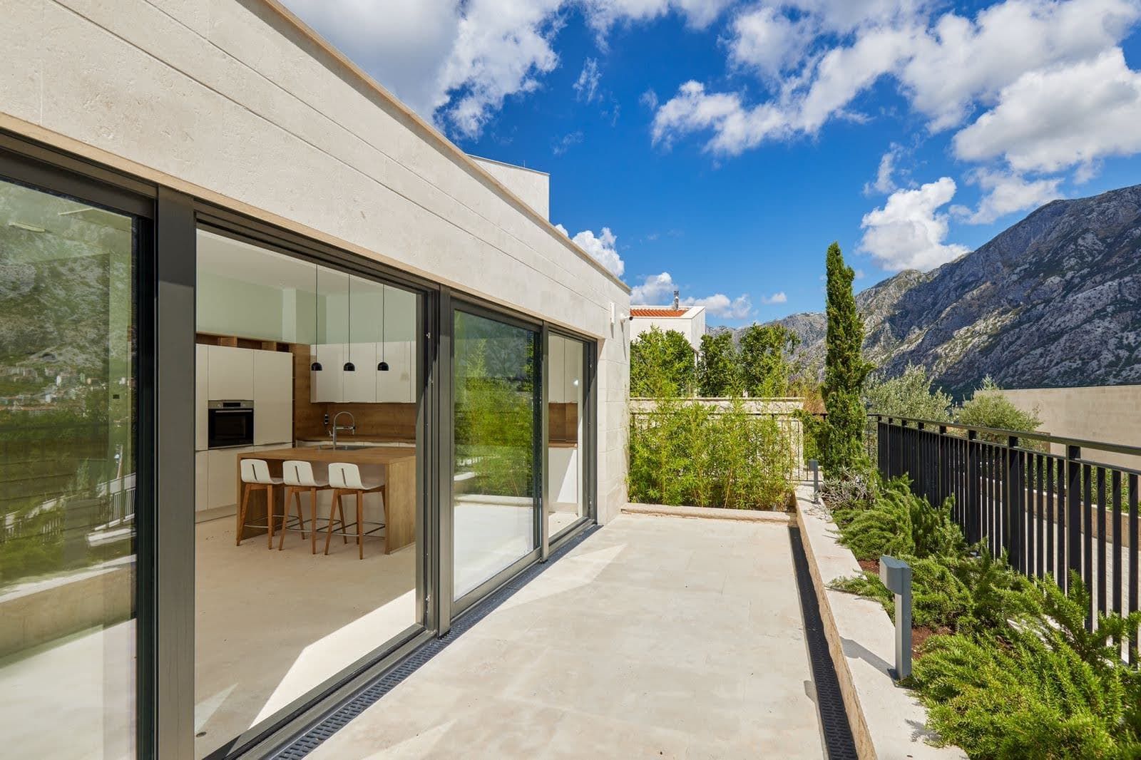 Terrace of a modern villa in Prčanj, Montenegro, with mountain views and access to a kitchen with panoramic glazing.