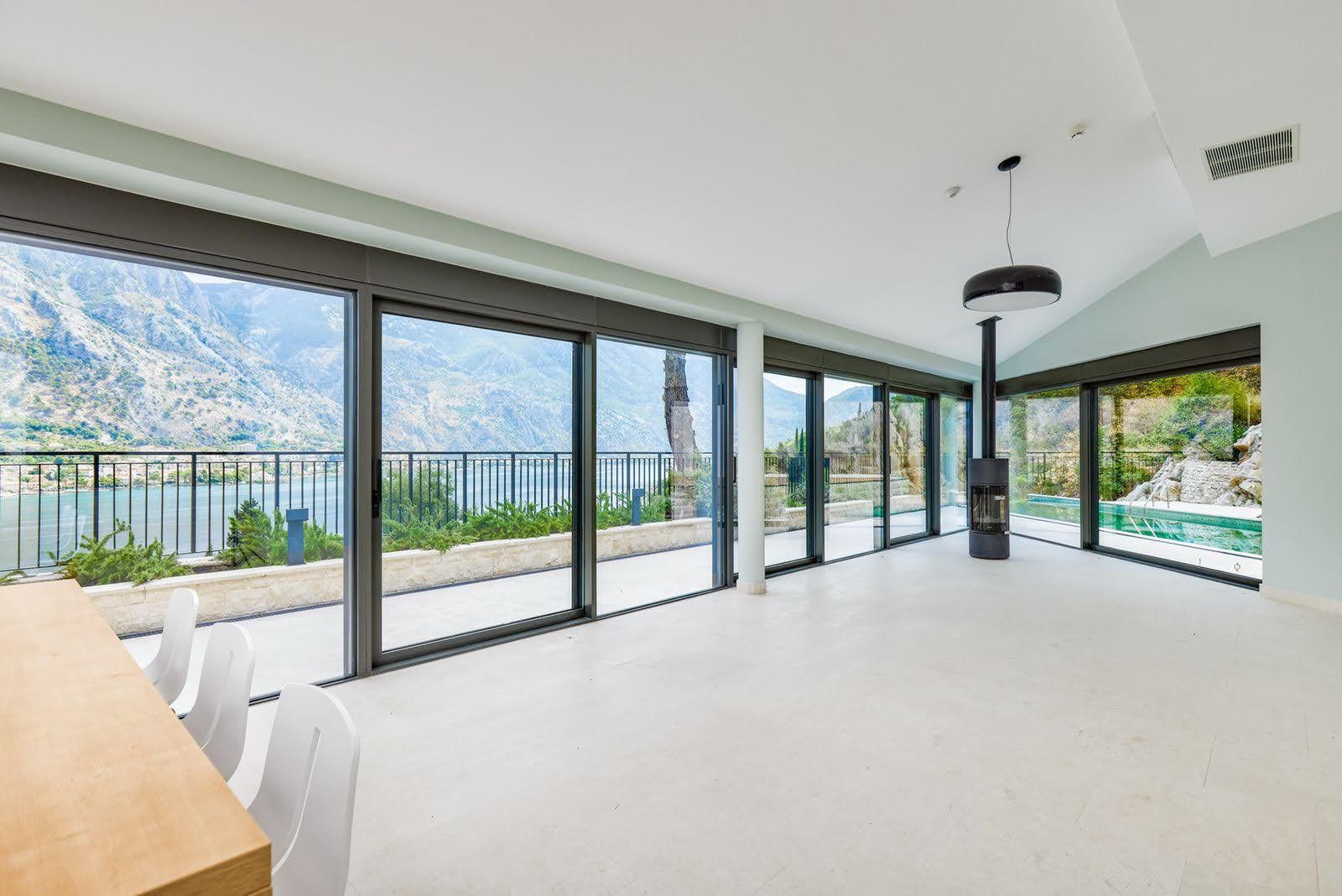 Villa living room in Prčanj, Montenegro: panoramic windows, views of the Bay of Kotor, a fireplace, and access to a private pool.
