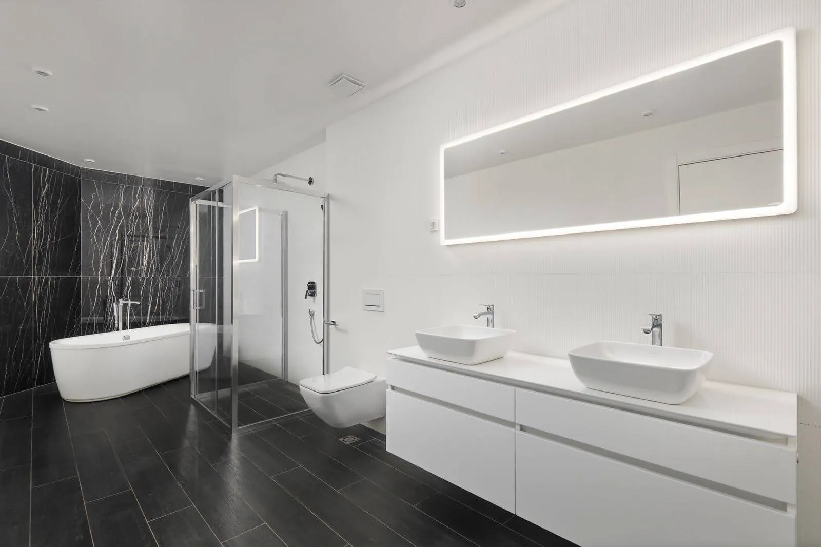 Modern bathroom with double vessel sinks, glass shower enclosure, freestanding tub, and black marble walls.