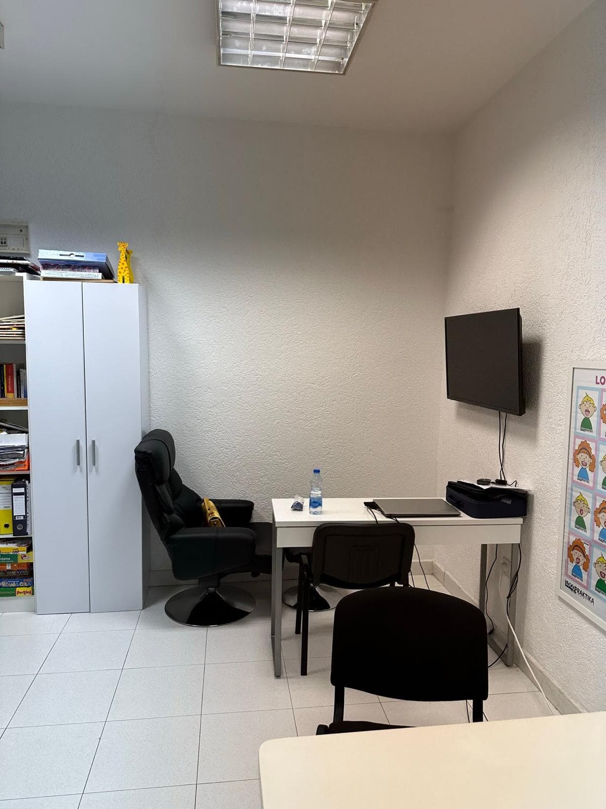 Office space in Bar, Montenegro: a workspace with a white desk, black chair, cabinet, and wall-mounted TV.