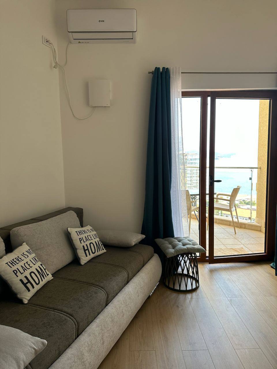 Living room in an apartment in Bečići, Montenegro: gray sofa, access to a terrace with a sea view, and a modern air conditioner.