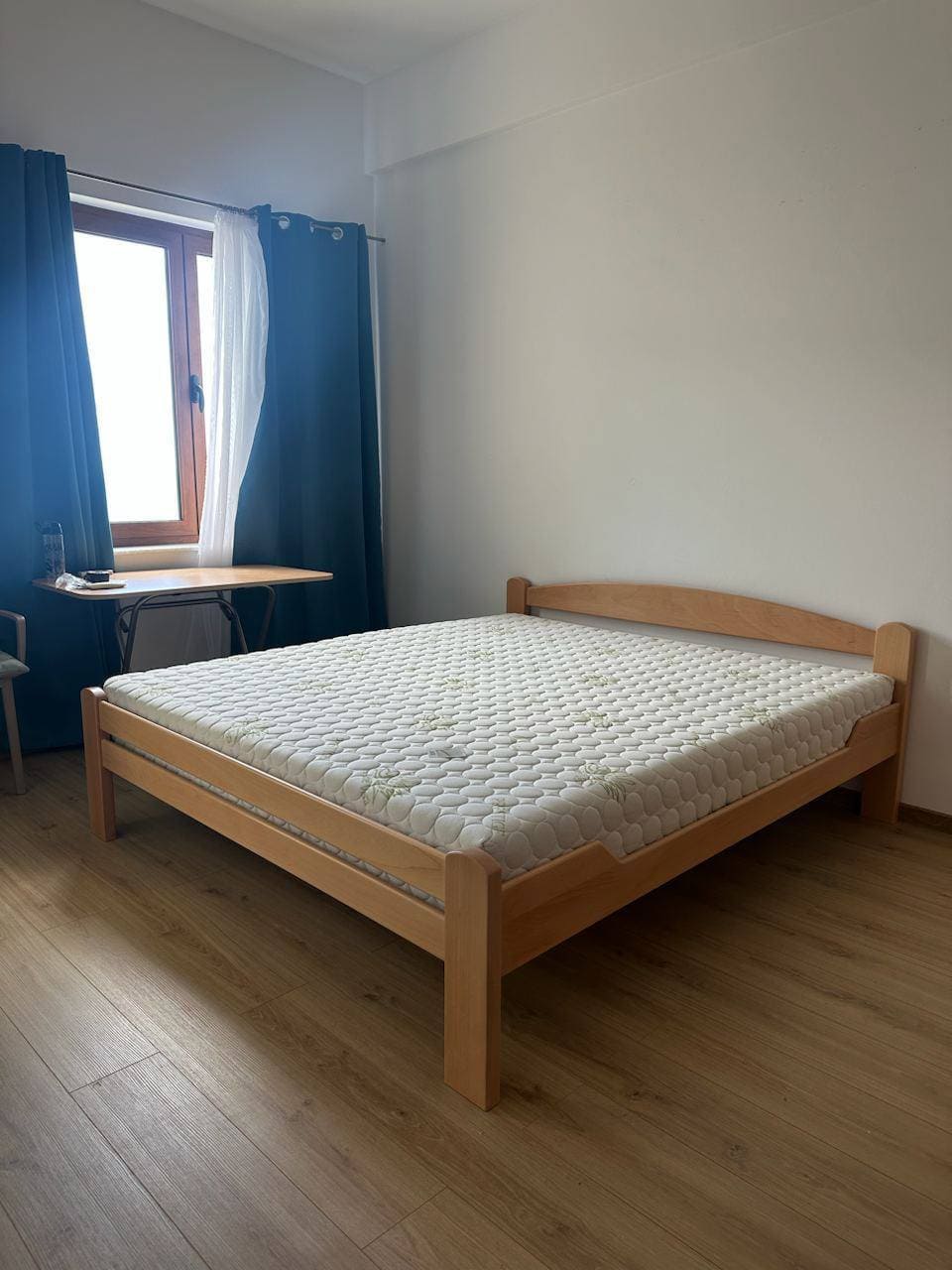 Bedroom with a double bed and light laminate flooring in an apartment in Bečići, Montenegro. Window with blue curtains.