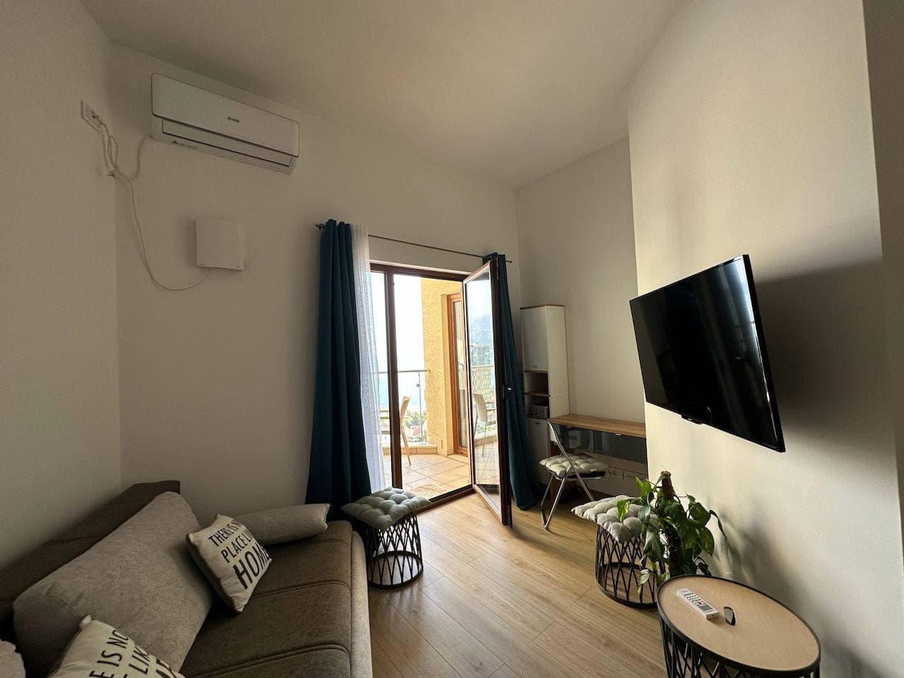 Cozy living room with balcony access in an apartment in Bečići, Montenegro: sofa, TV, air conditioning, and light-colored finishes.