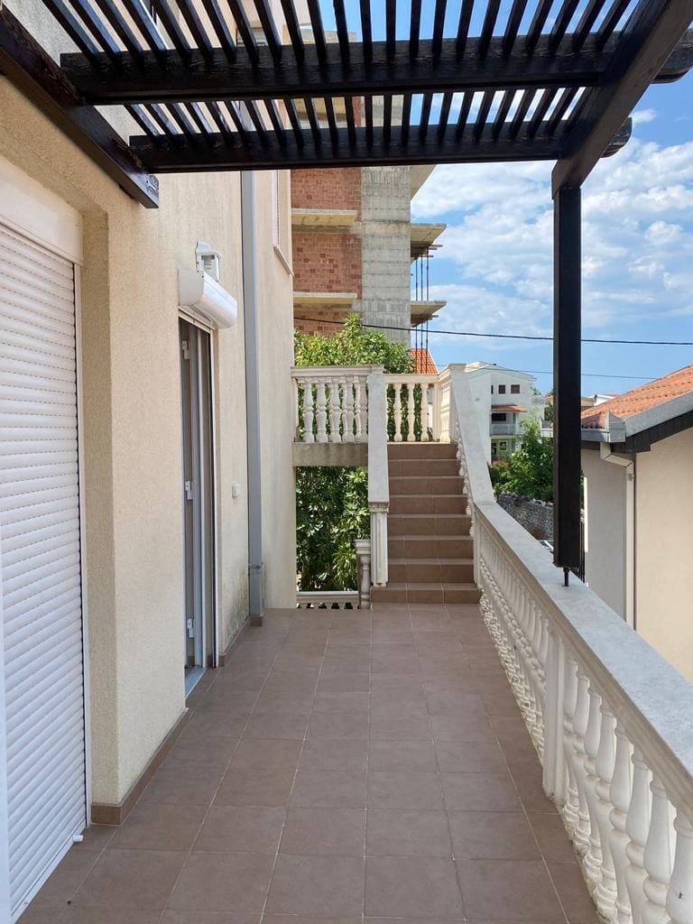 Spacious terrace with a canopy and staircase in the house, Dobra Voda, Montenegro. View of neighboring buildings and greenery.