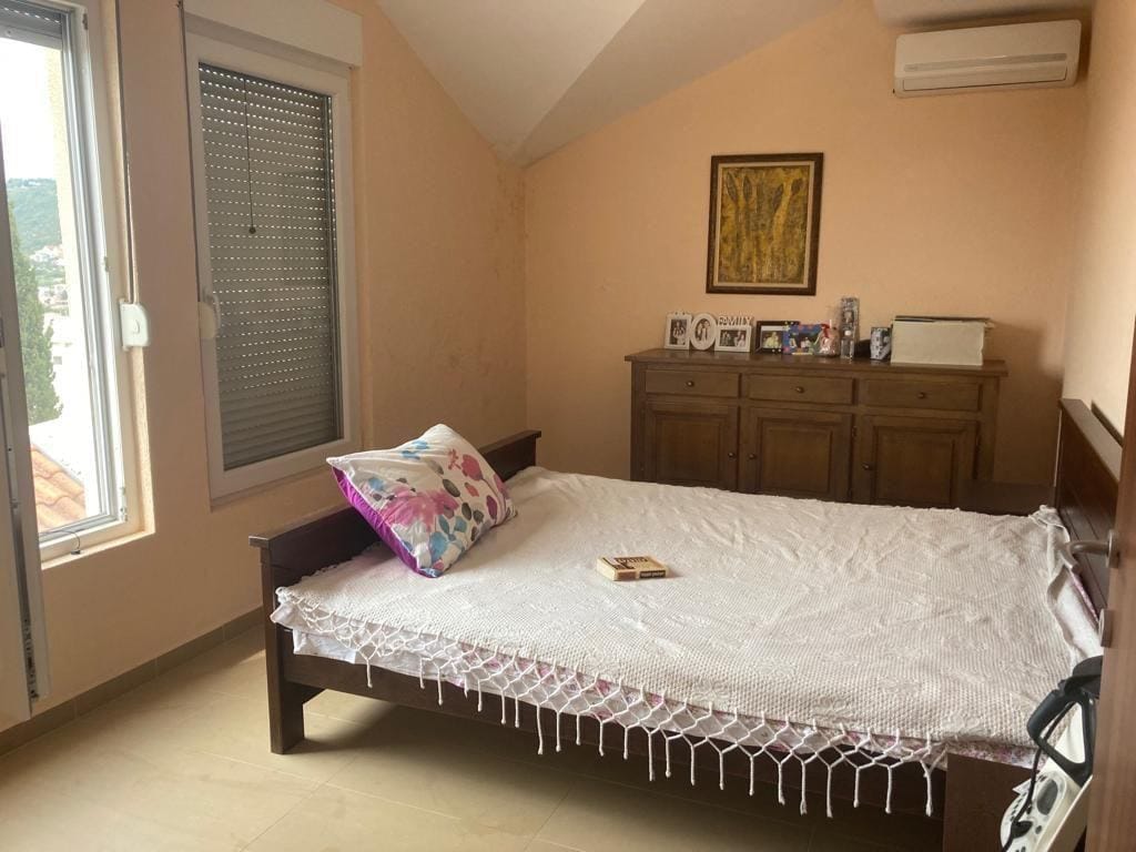 Cozy bedroom with a double bed and a wooden dresser in a house, Dobra Voda, Montenegro. Mountain view from the window.