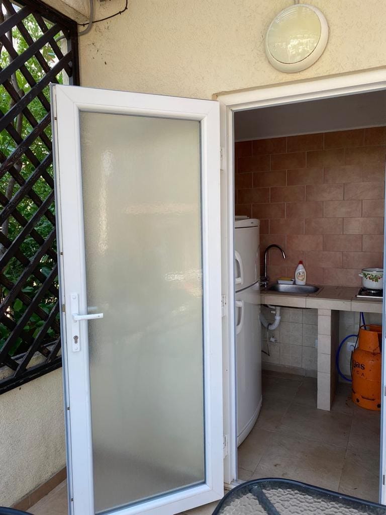 Summer kitchen with a refrigerator and gas stove in the house, Dobra Voda, Montenegro. Access to the terrace through a plastic door.