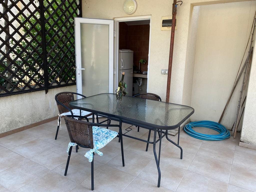Cozy terrace with dining area in a house, Dobra Voda, Montenegro: glass table, wicker chairs, and access to the kitchen.