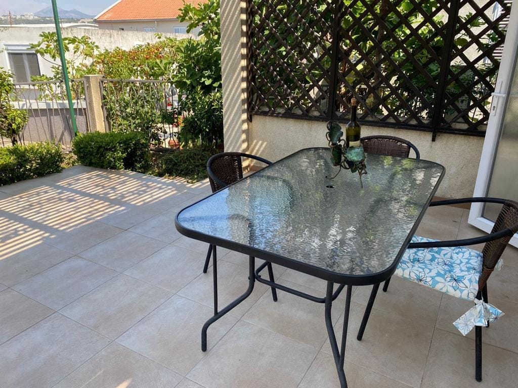 Cozy terrace with dining area in a house, Dobra Voda, Montenegro: glass table, wicker chairs, and a view of the garden.