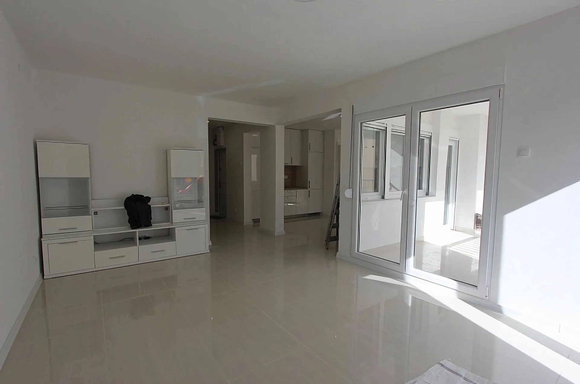 Bright room with a white glossy cabinet and glass balcony door. The floor has light-colored tiles.