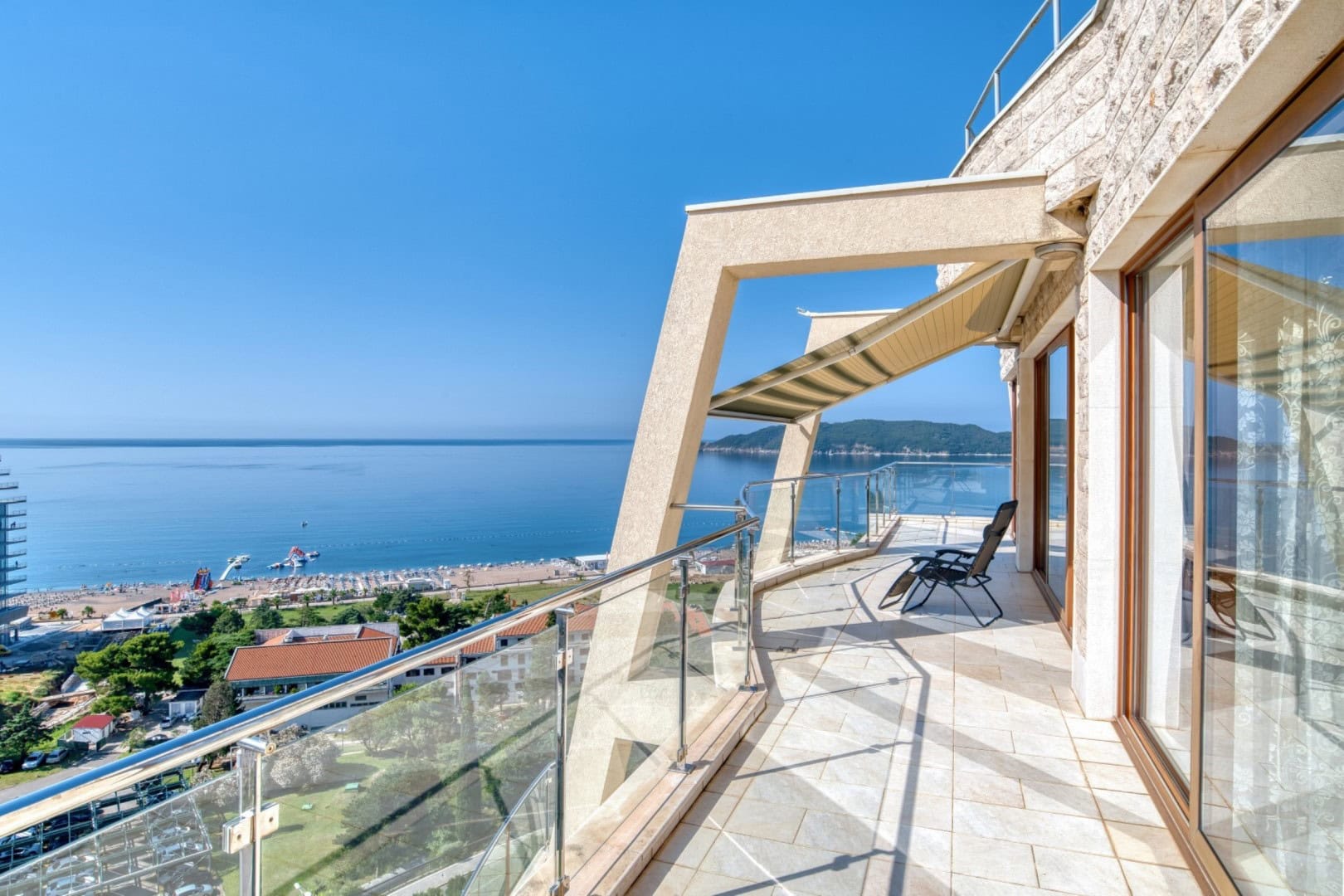 Spacious penthouse terrace in Bečići, Montenegro, featuring panoramic sea views, glass railings, and a sun lounger.
