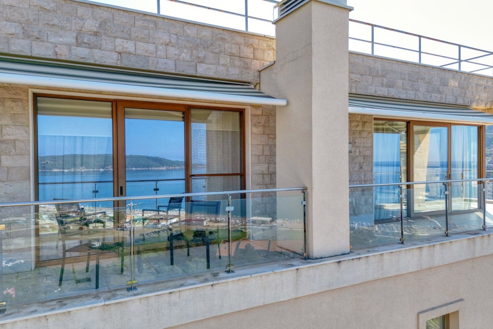 Spacious penthouse balcony in Bečići, Montenegro, featuring panoramic sea views, glass railings, and outdoor furniture.