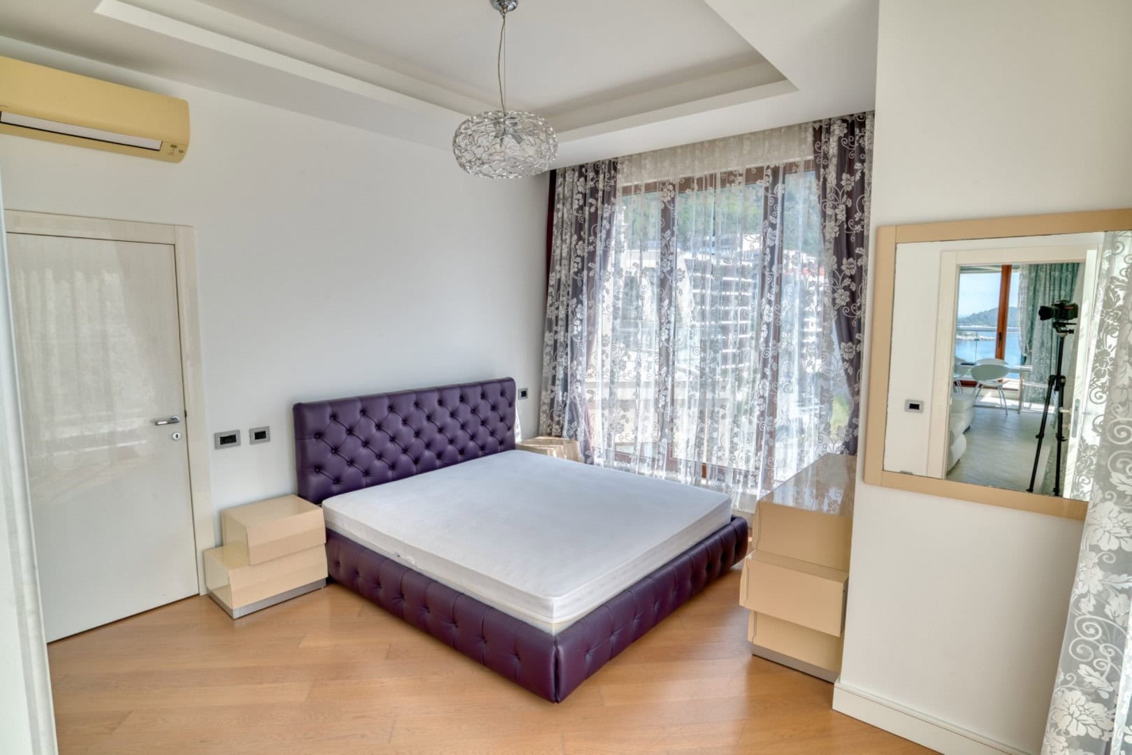 Bedroom in a penthouse in Becici, Montenegro: double bed with a purple headboard, panoramic windows, and a sea view.