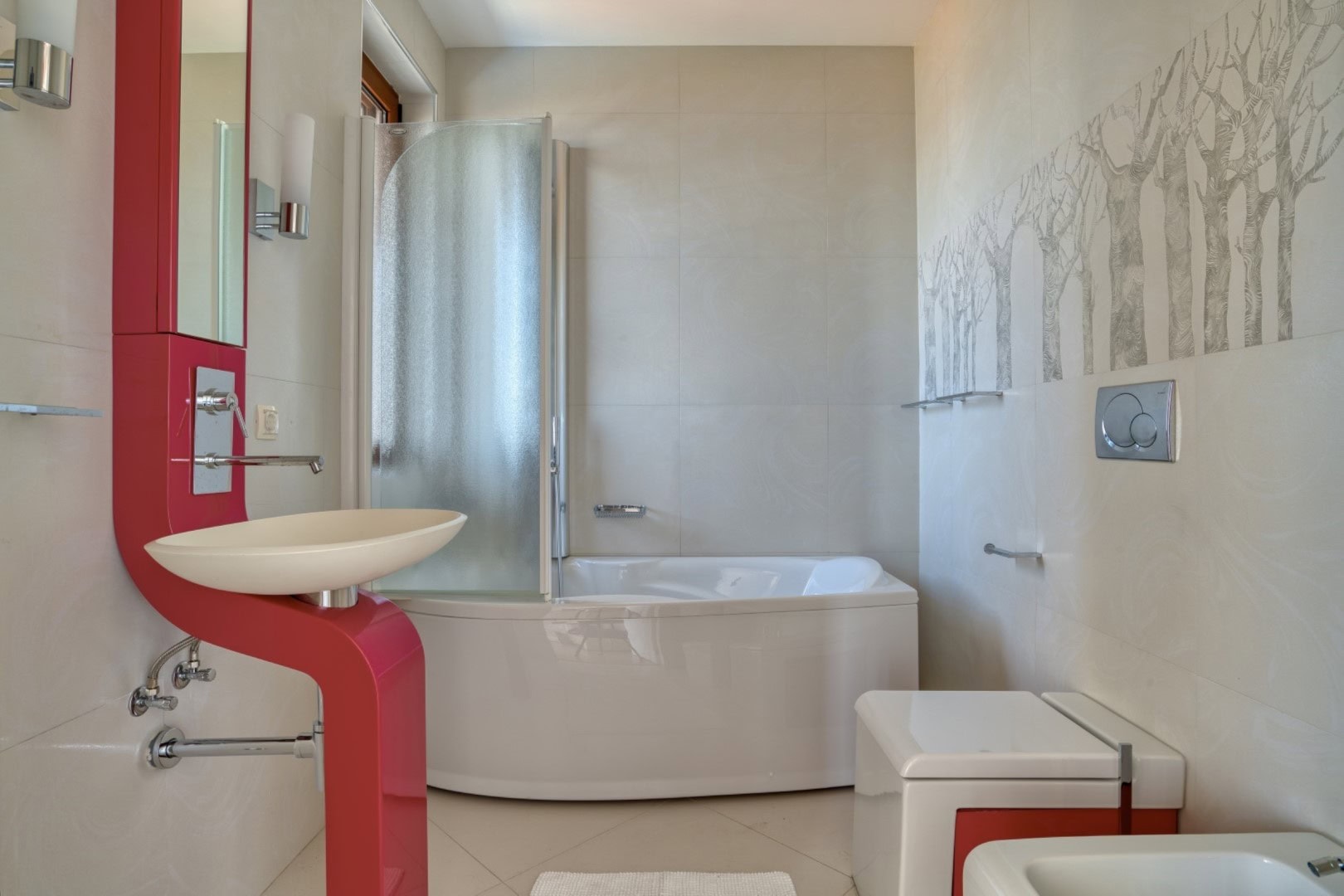Modern bathroom in a penthouse in Becici, Montenegro: white sanitary ware, corner bathtub, and vibrant red furniture.