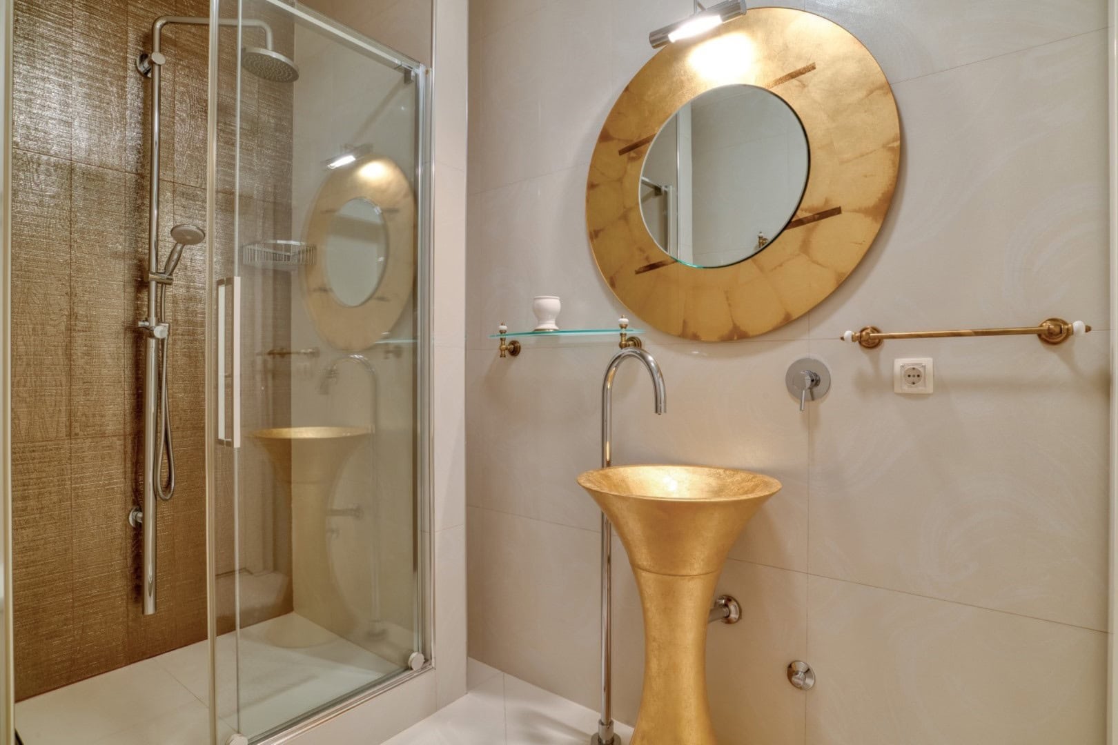 Bathroom in a penthouse in Bečići, Montenegro: gold sink, round mirror, and a finished shower cabin.