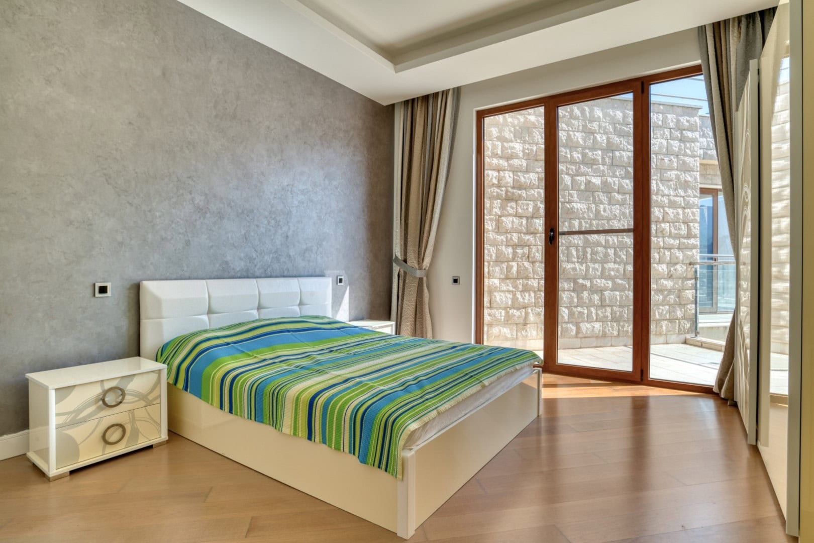 Bedroom in a penthouse in Bečići, Montenegro: double bed, panoramic windows, and access to a stone-finished terrace.