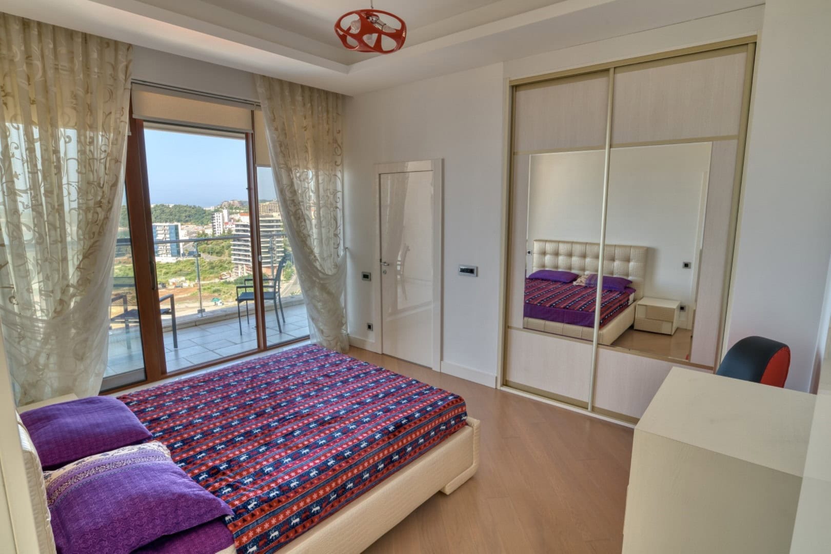 Bedroom in a penthouse in Becici, Montenegro: double bed, mirrored sliding-door wardrobe, and access to a terrace with a view.