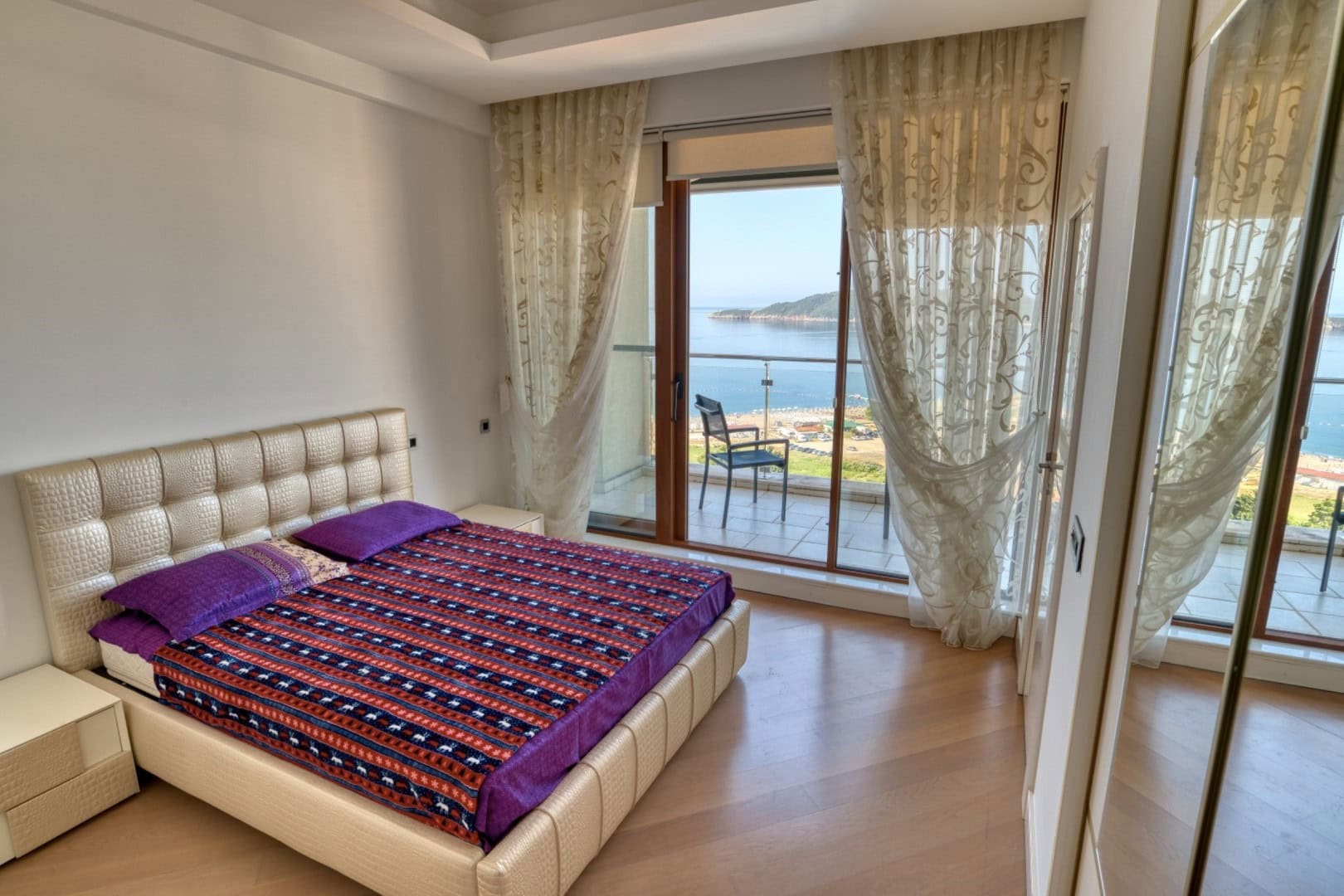 Bedroom in a penthouse in Bečići, Montenegro: double bed, panoramic windows, and a balcony with a view of the sea and the beach.