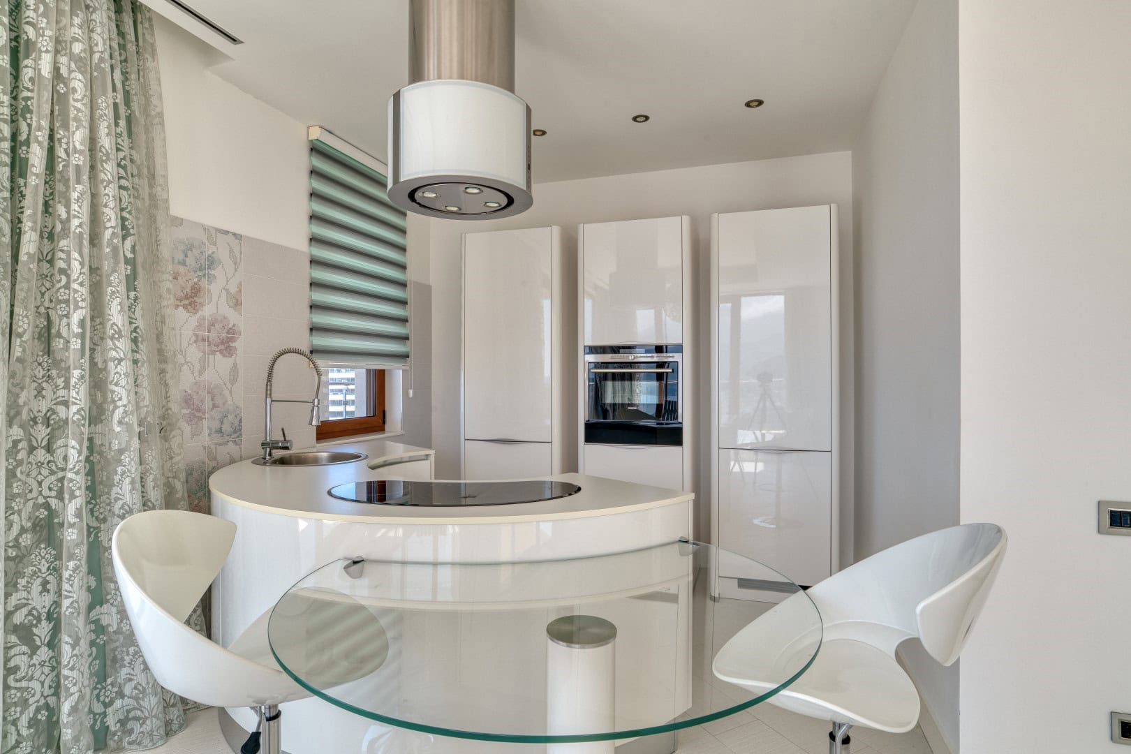 Modern white kitchen with an island and a glass table in a penthouse, Becici, Montenegro.